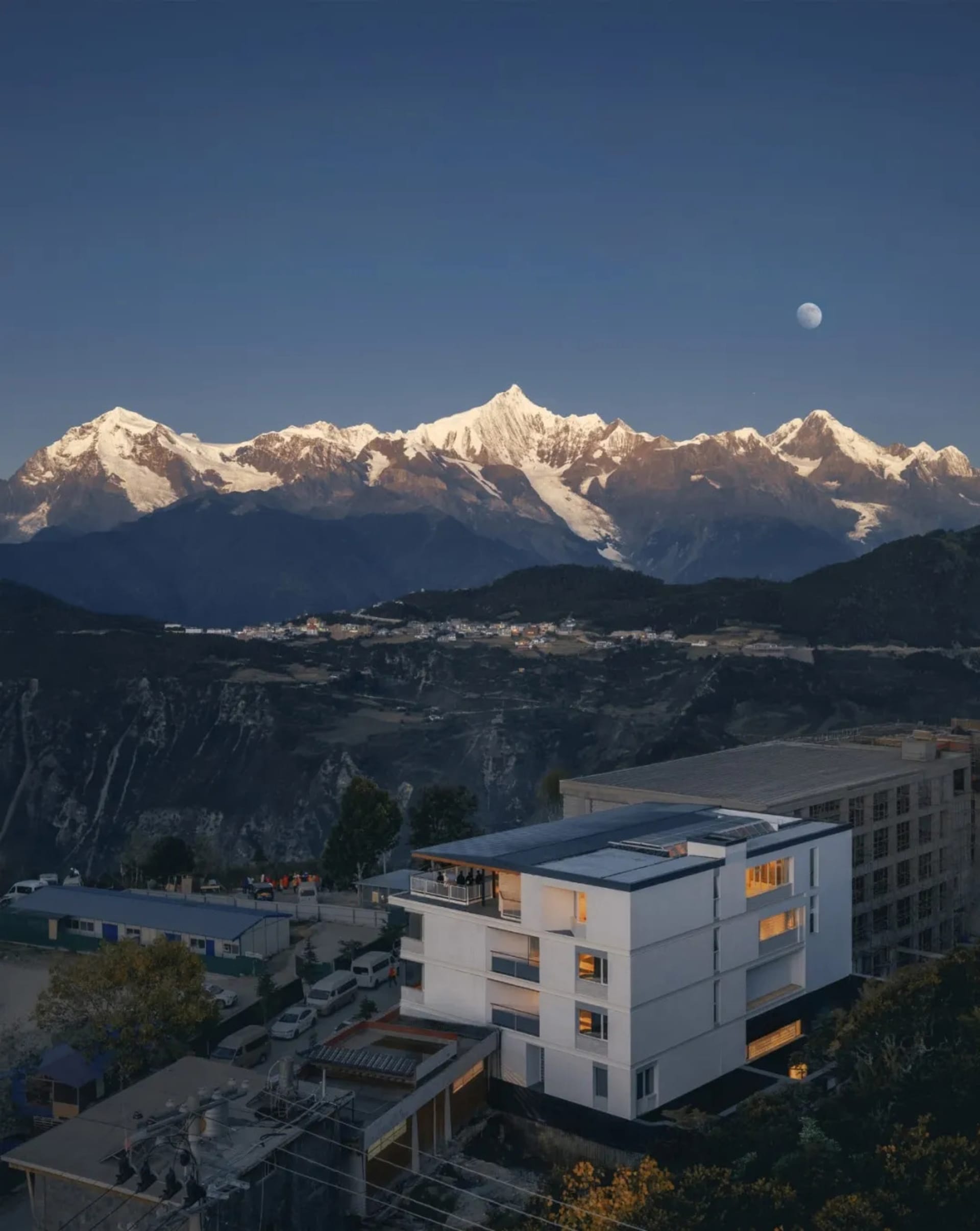 A serene mountain house with a modern exterior, featuring a black roof and large windows, surrounded by a picturesque landscape with mountains in the background
