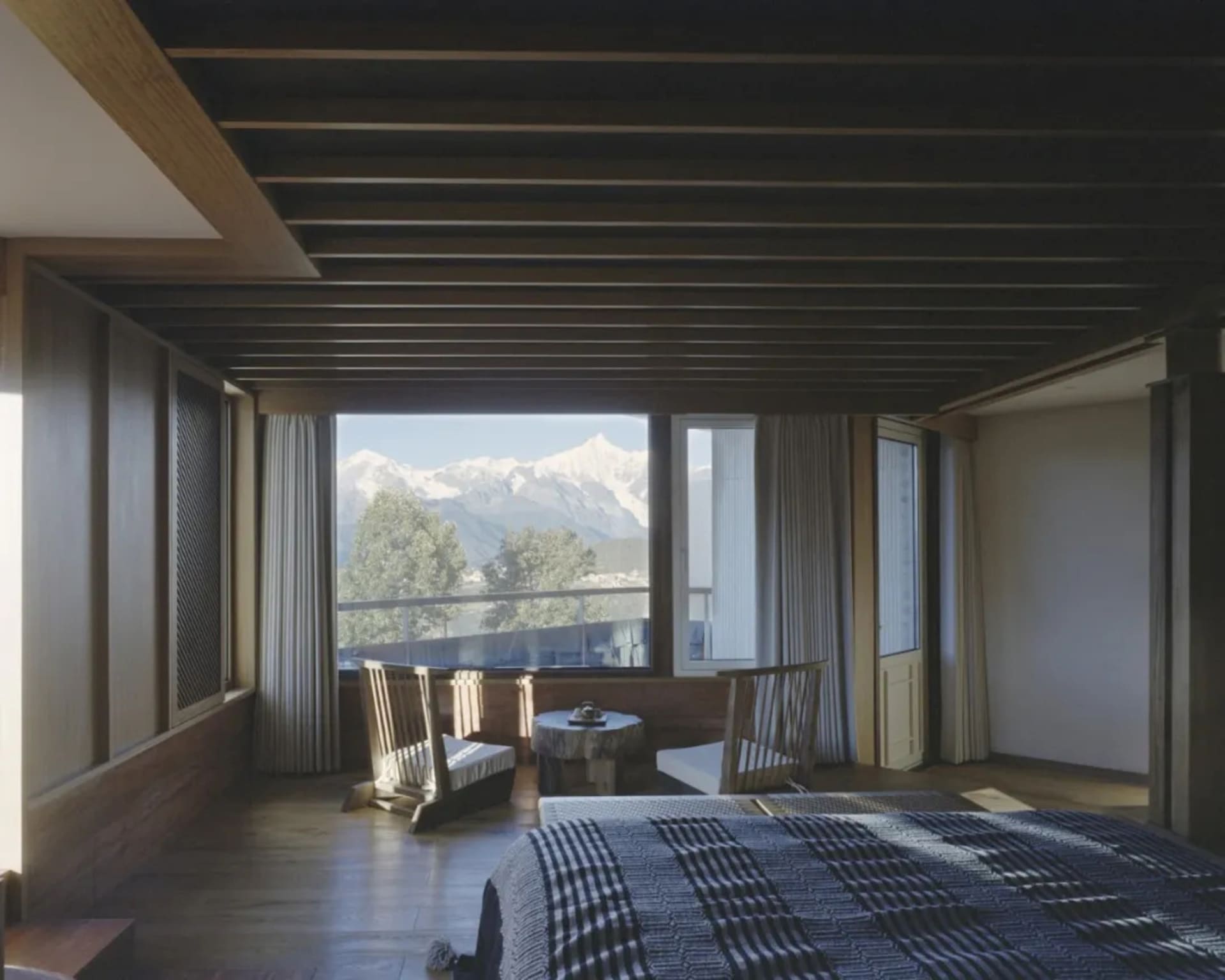 Cozy bedroom with a wooden floor, wooden ceiling, a bed with a plaid blanket, a chair, and a dining table in the corner, with natural light coming in through the window