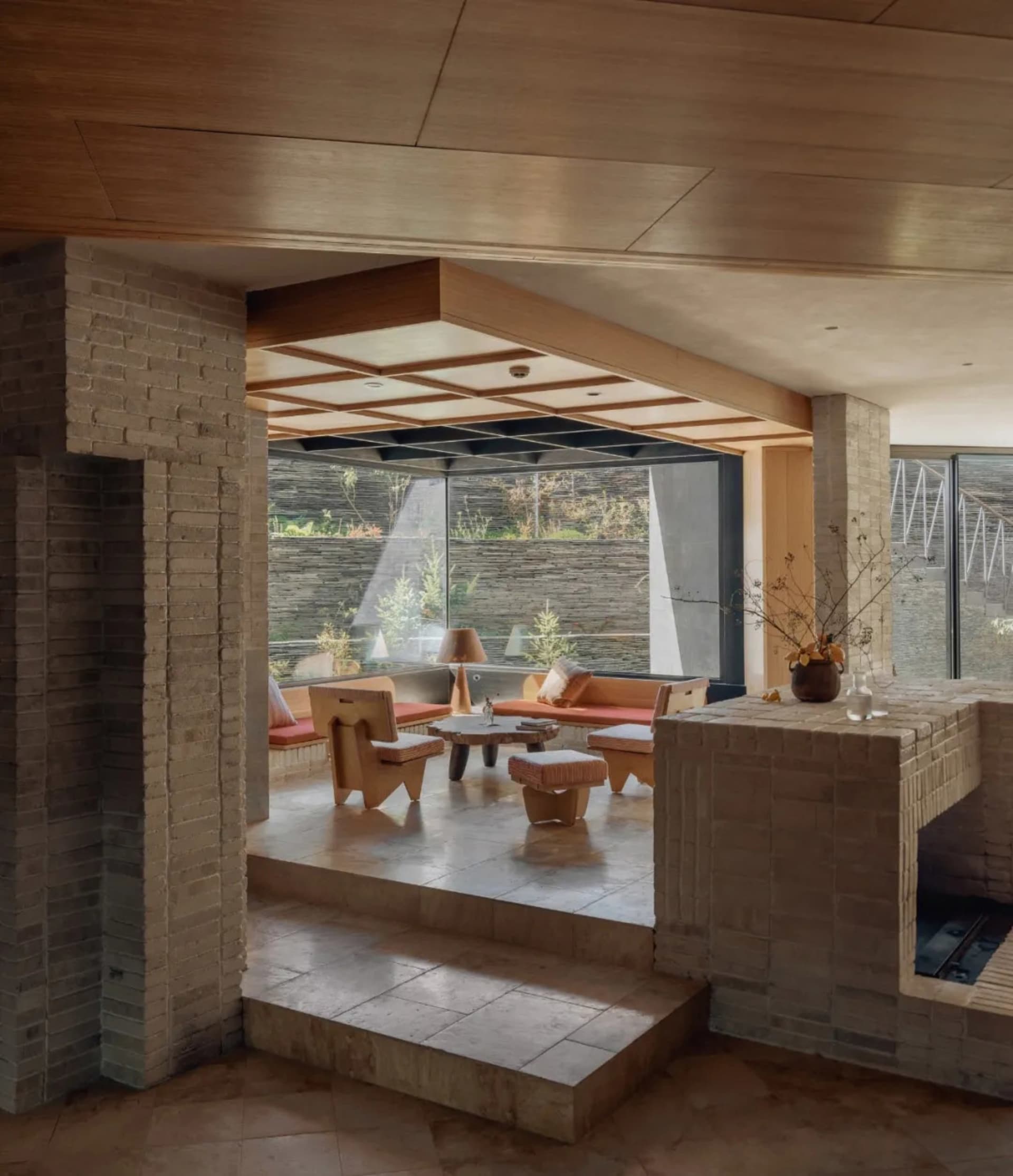 Warm and inviting living room with a stone fireplace, brick wall, stone floor, and stone countertop, furnished with a couch, chair, and dining table, with potted plants and vases adding to the ambiance
