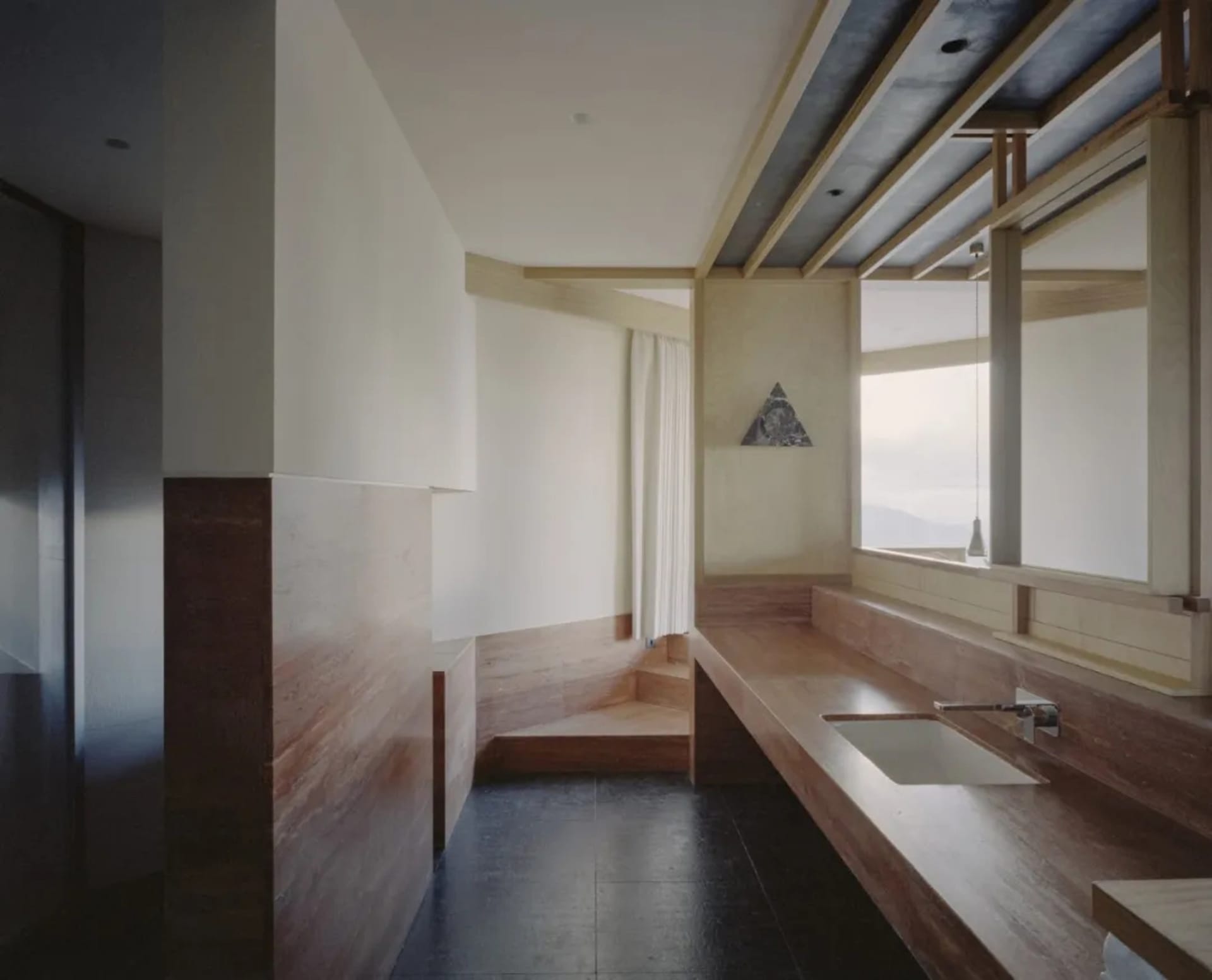 A minimalist bathroom with a wooden bench, sink, and window, featuring a dimly lit, warm, and natural atmosphere
