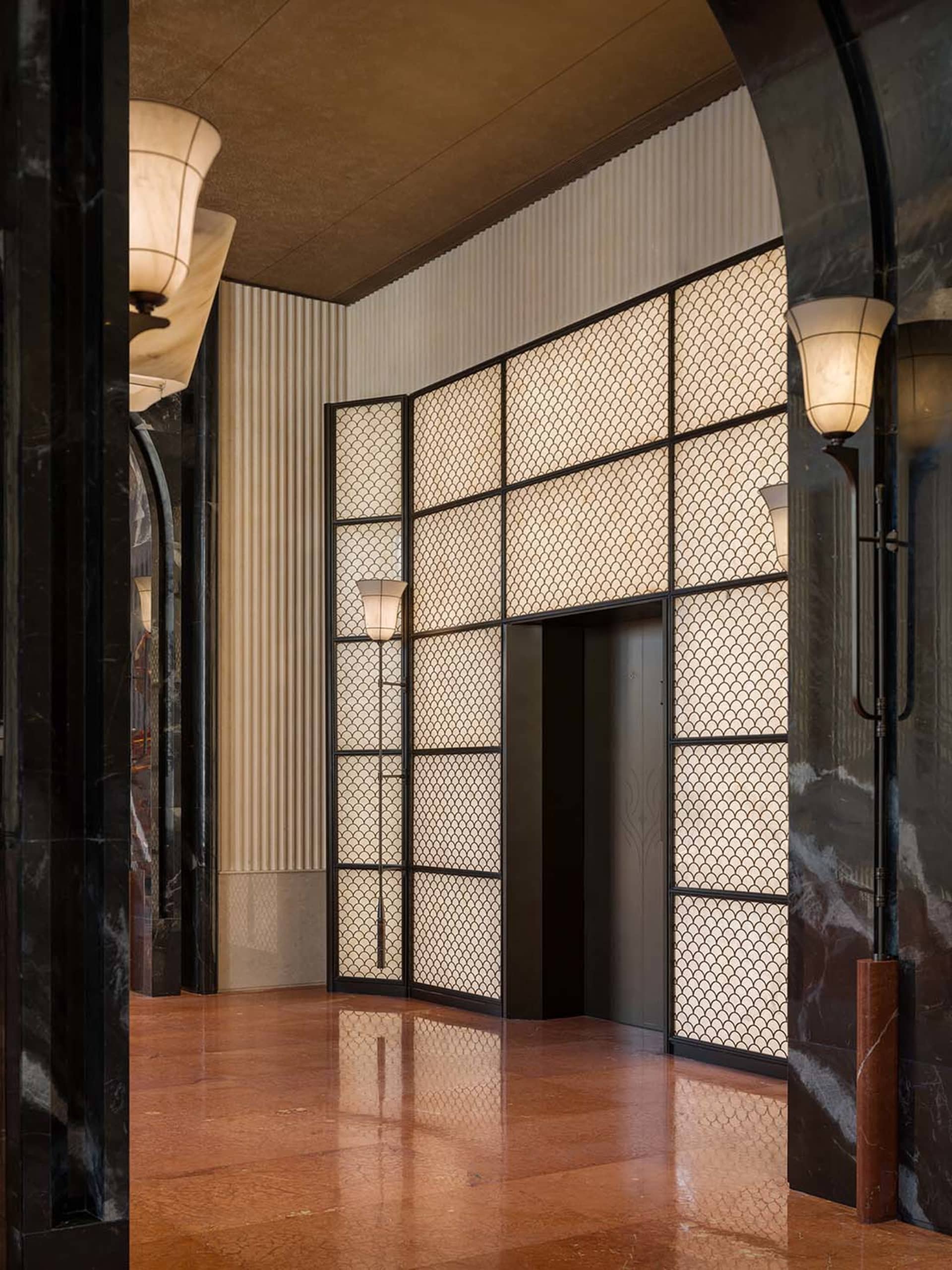 A modern hallway with a black and white color scheme, lined with doors and lights, featuring a doorway to a larger room, with a dim atmosphere