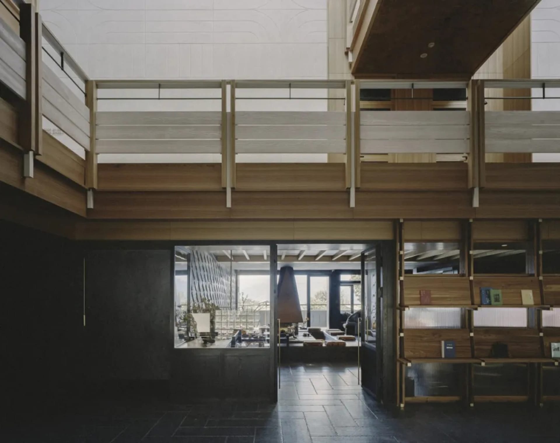 Large open living room with a wooden floor, balcony, staircase, and modern furniture, featuring a fireplace and natural light from windows