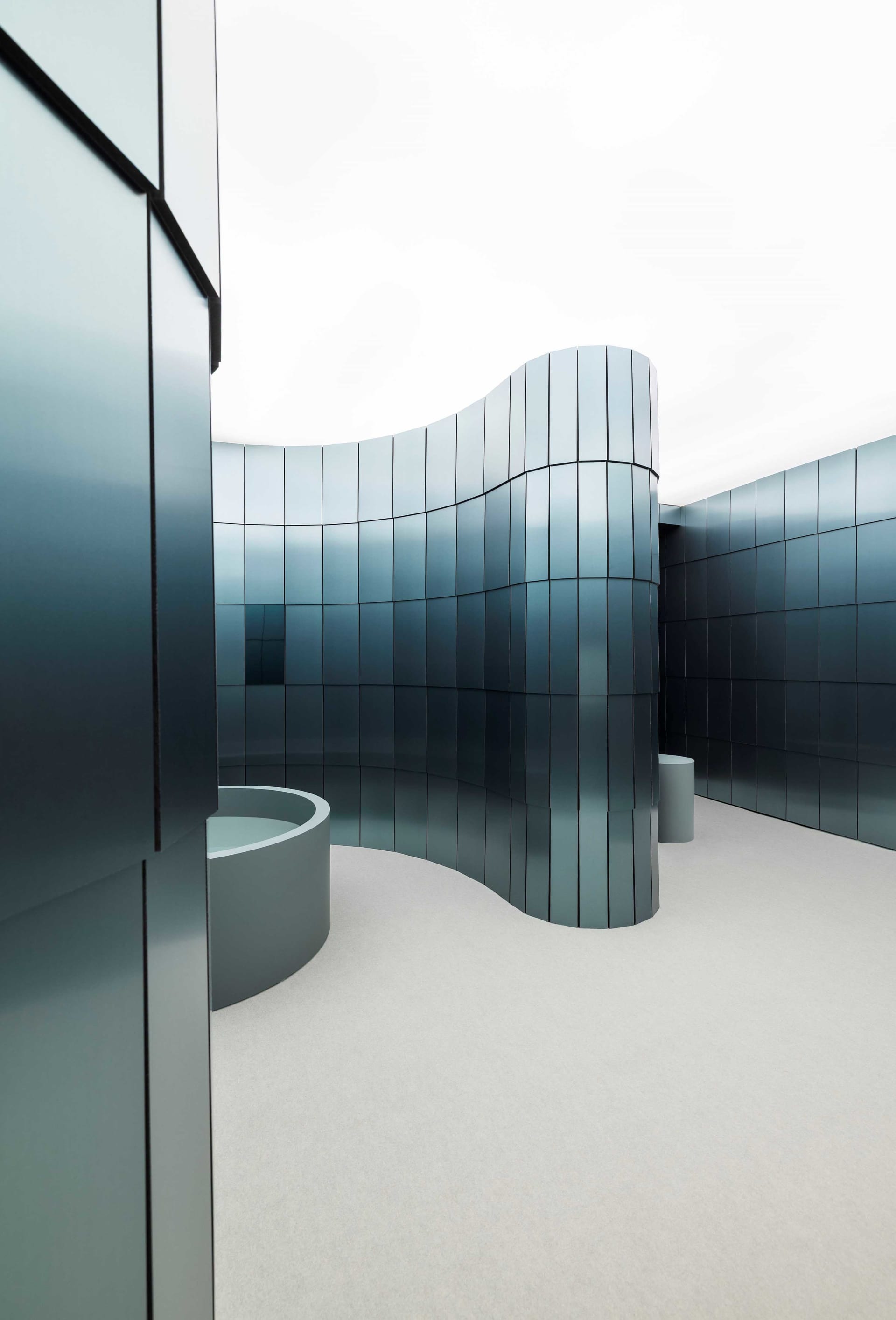 Modern building with a curved design, large glass wall, and blue interior walls, surrounded by natural light and a well-lit atmosphere