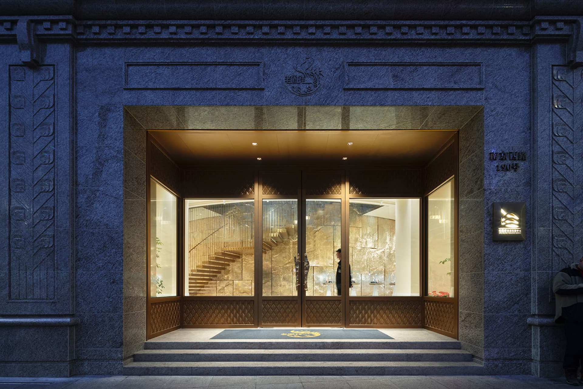 A grand entrance with a large doorway featuring a golden design and a wooden staircase, set in a sophisticated architectural space