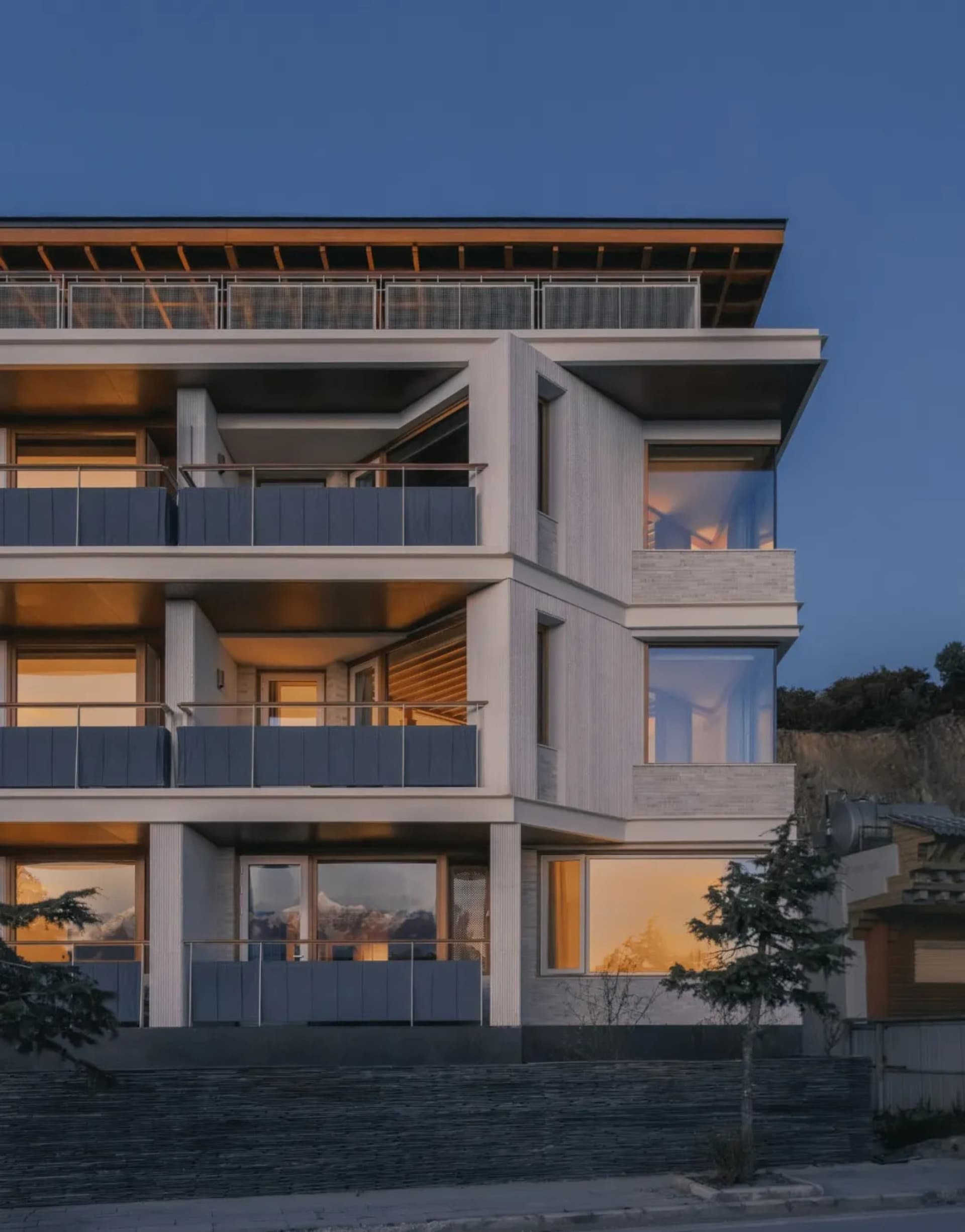 A modern building with a mix of white and grey colors, featuring numerous windows and artificial lighting, creating a clean and sophisticated appearance