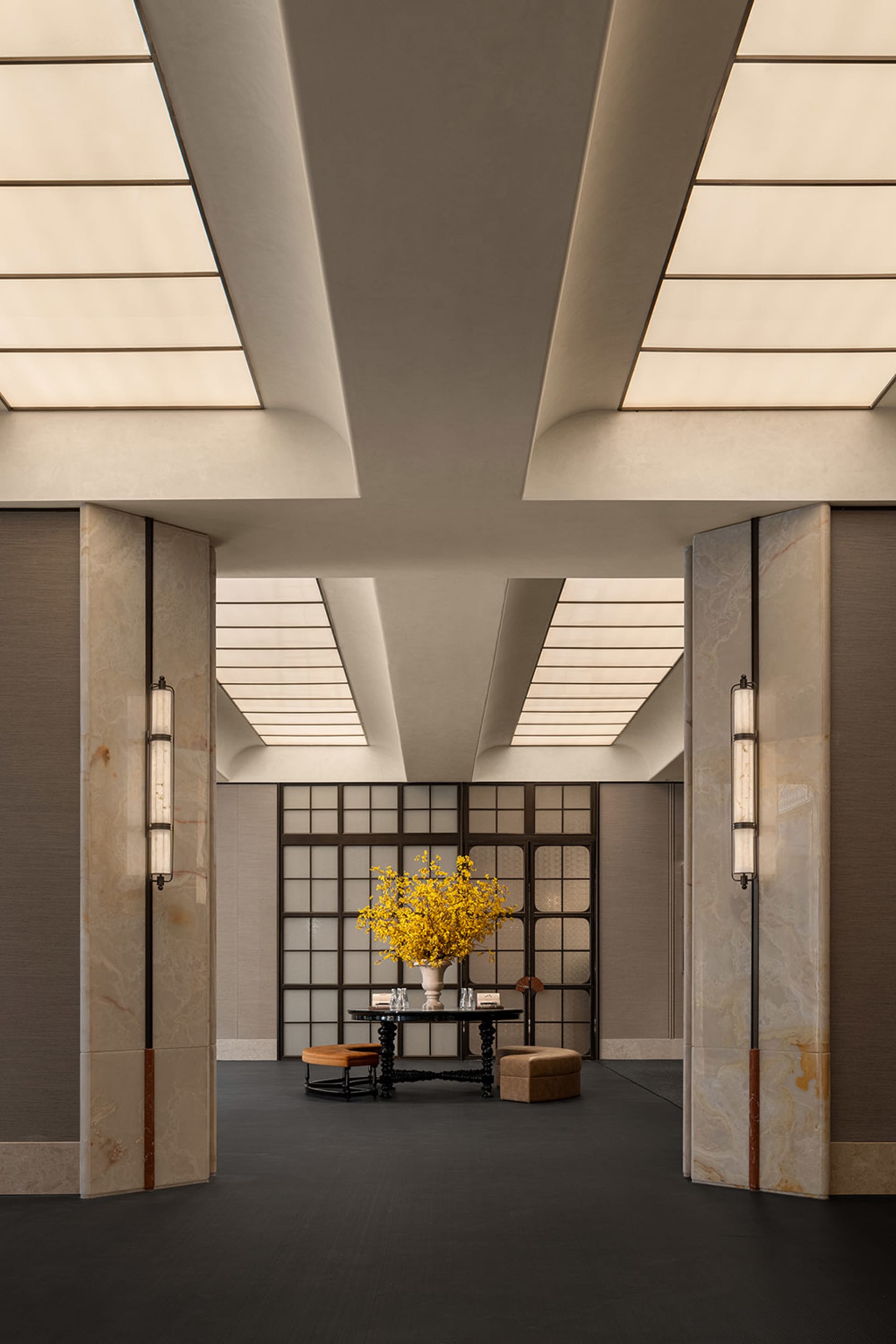 A dimly lit lobby with a hardwood floor, a white ceiling, and a large vase of flowers on a table