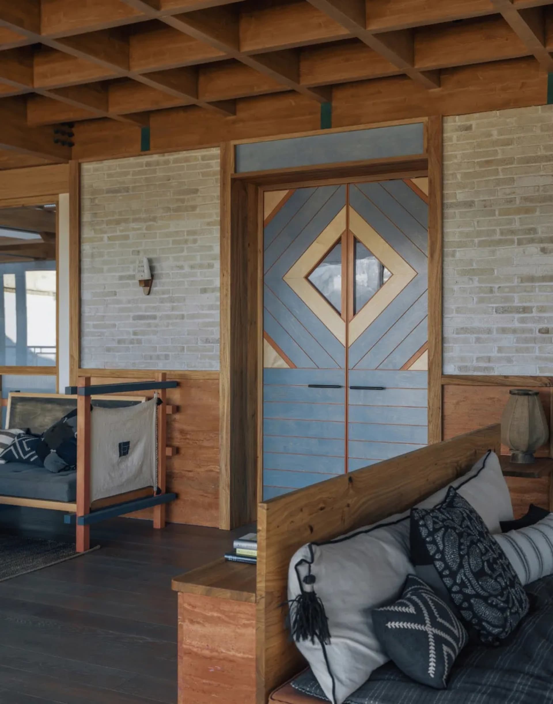 Comfortable living space with a wooden floor, a blue door, a wooden bench, a couch, a chair, a book, and a vase, well-lit and inviting