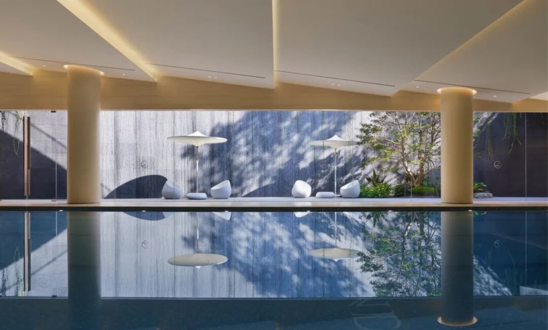 A serene pool area surrounded by a stone wall, with three white lamps providing soft lighting and a reflective pool surface