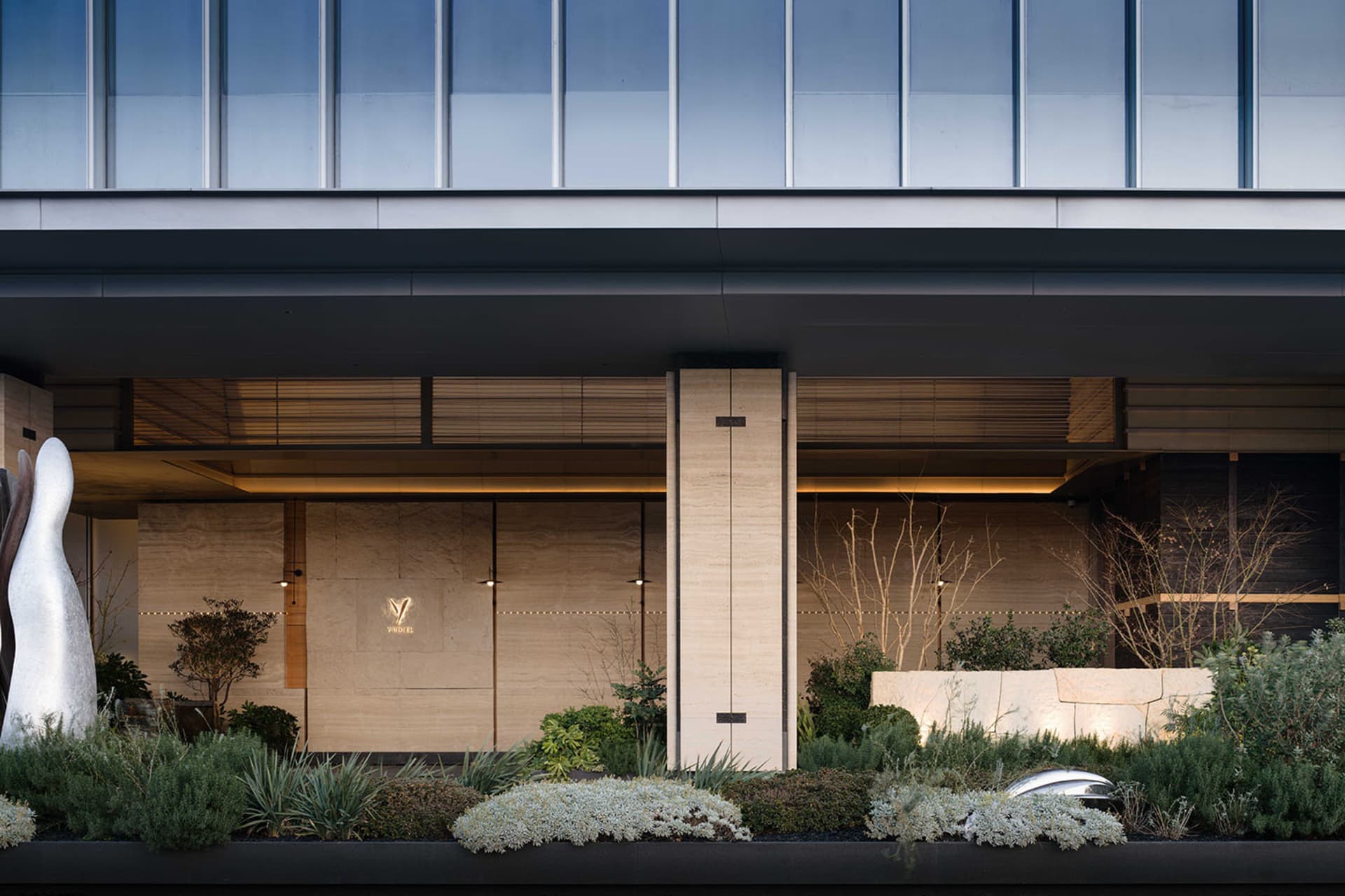 A modern stone building with a glass front, well-lit and inviting, with a bench in front suggesting a public or commercial space