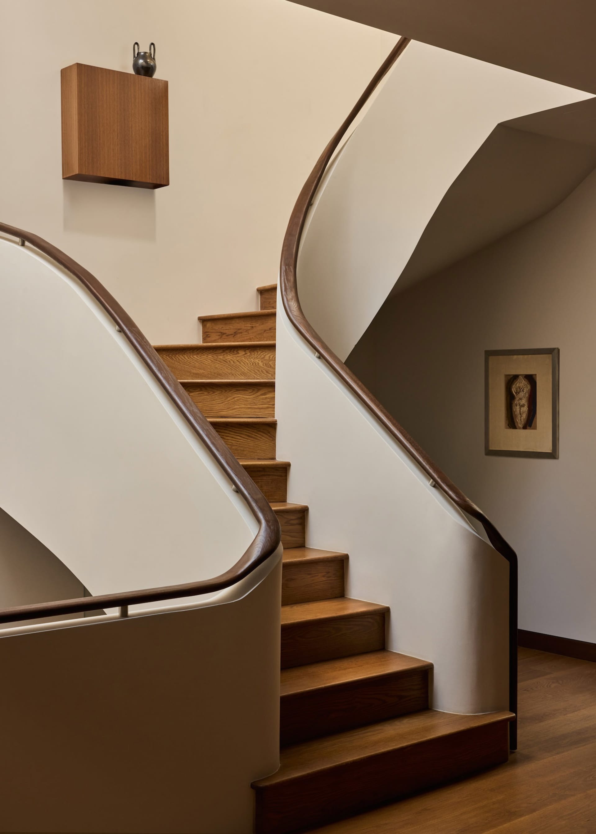 A modern staircase with a wooden railing in a residential hallway, bathed in natural light
