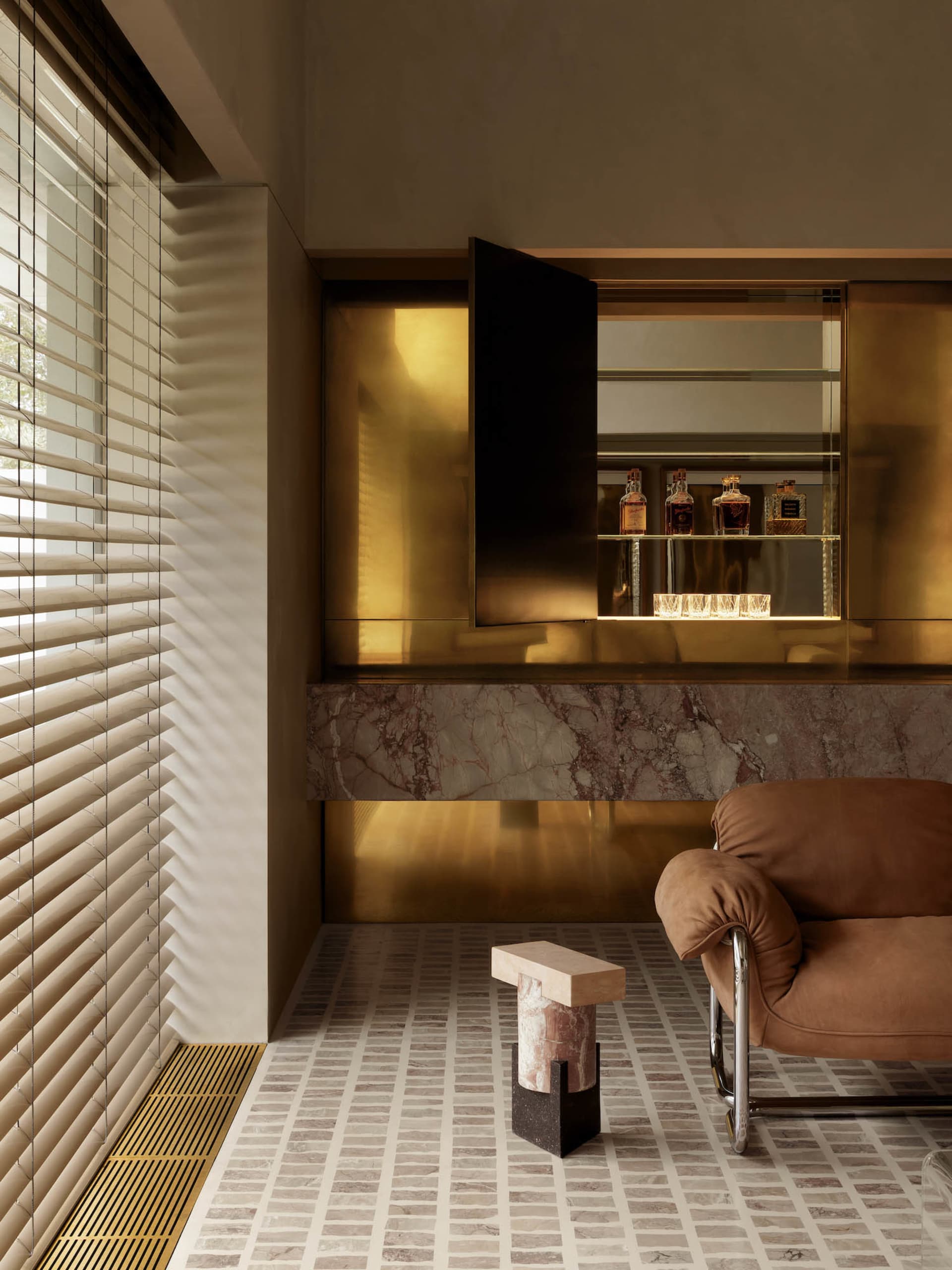 Warm and inviting living room with a marble floor, gold wall, and brown chair, featuring a dining table with bottles and a vase on the floor