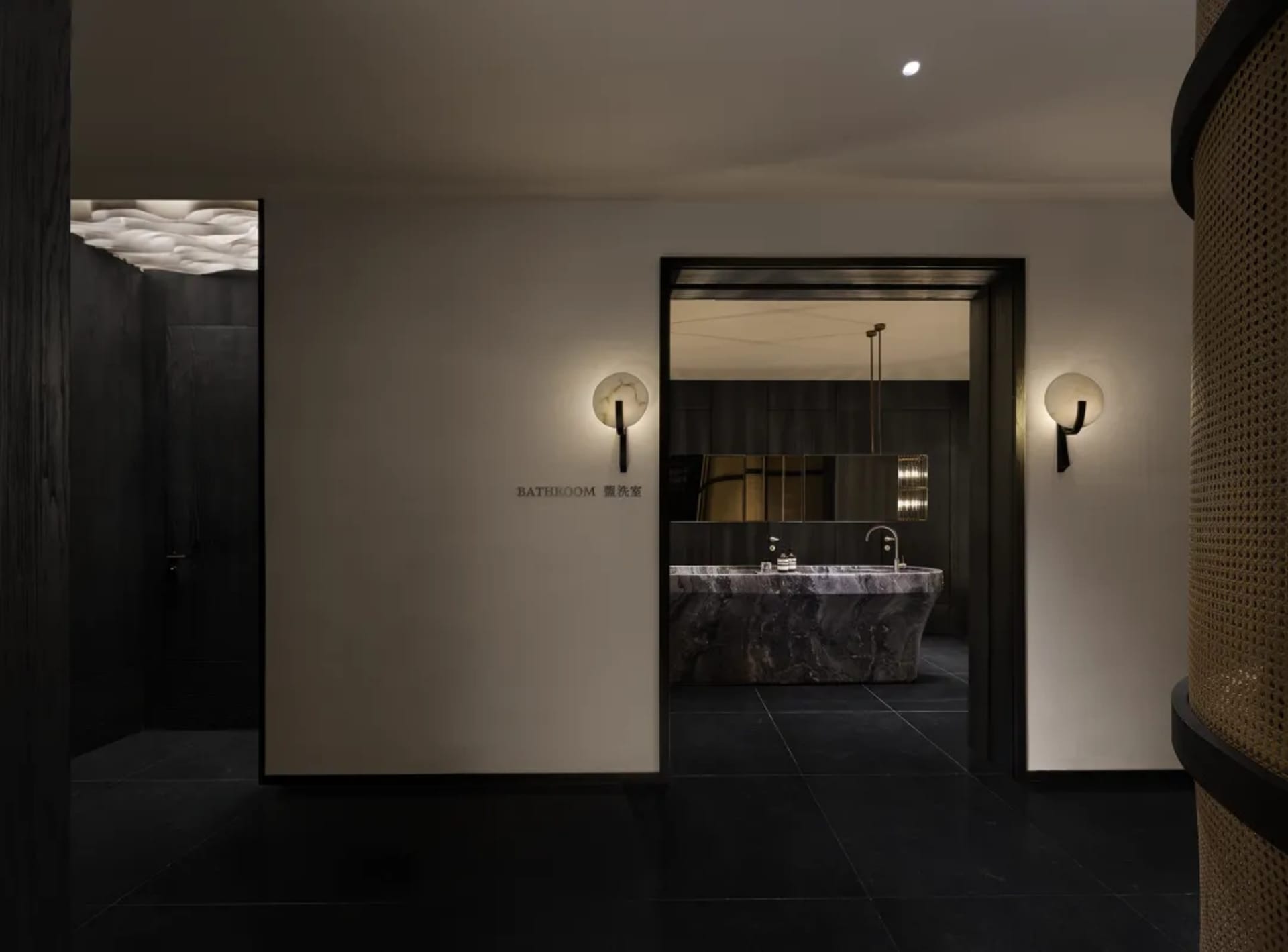 A modern bathroom with a white sink, mirror, and black tile floor, set in a dimly lit space