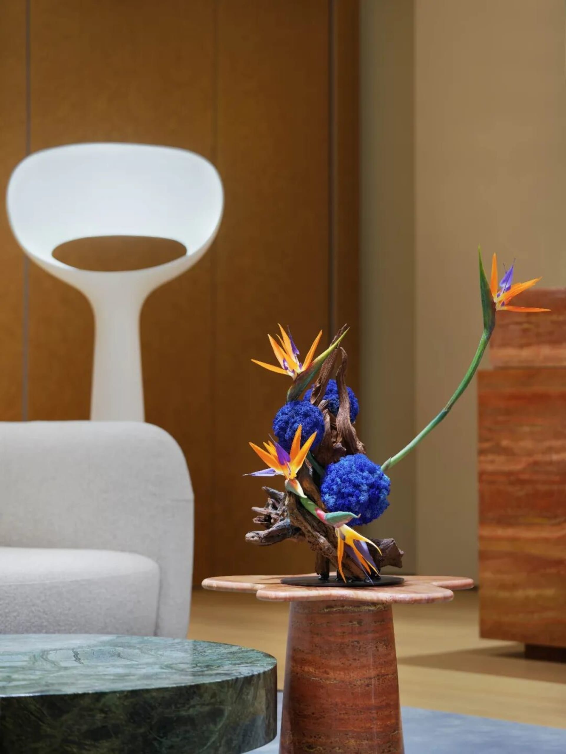 A modern living room with a couch, chair, and small table featuring a vase with flowers, set against a neutral background with soft, diffused lighting