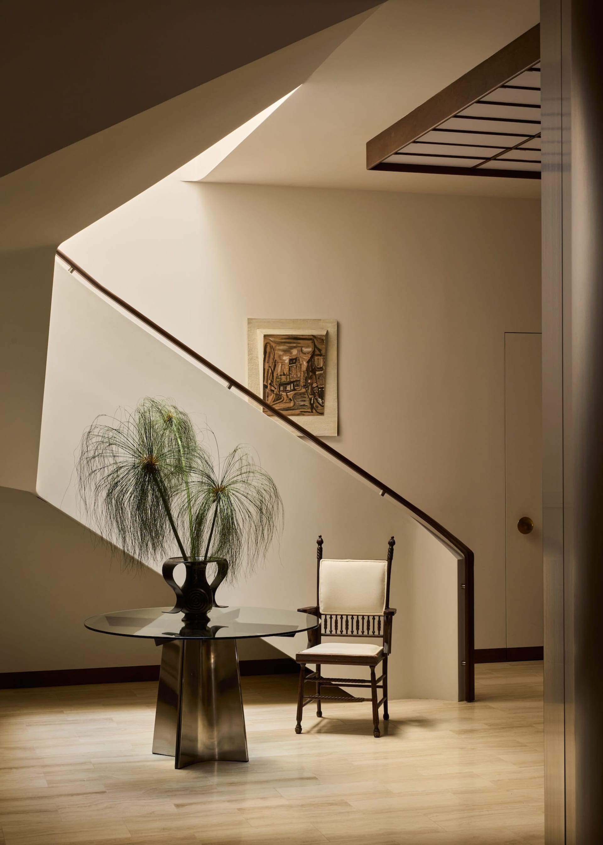 Cozy modern living space with a wooden staircase, glass table, and potted plant, set against white walls and a wooden floor