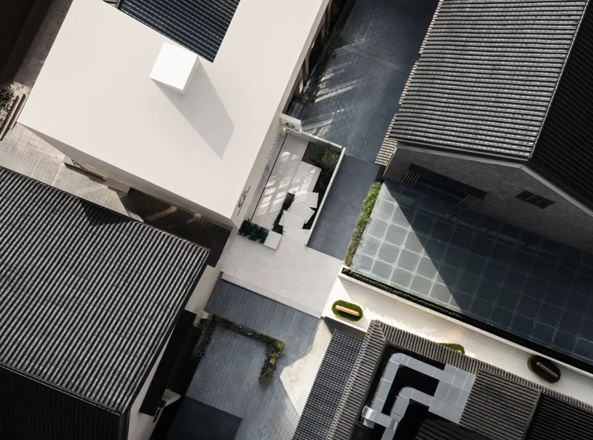 A modern building with a white concrete facade, a balcony, and a patio, surrounded by a courtyard, with natural sunlight and a bright atmosphere