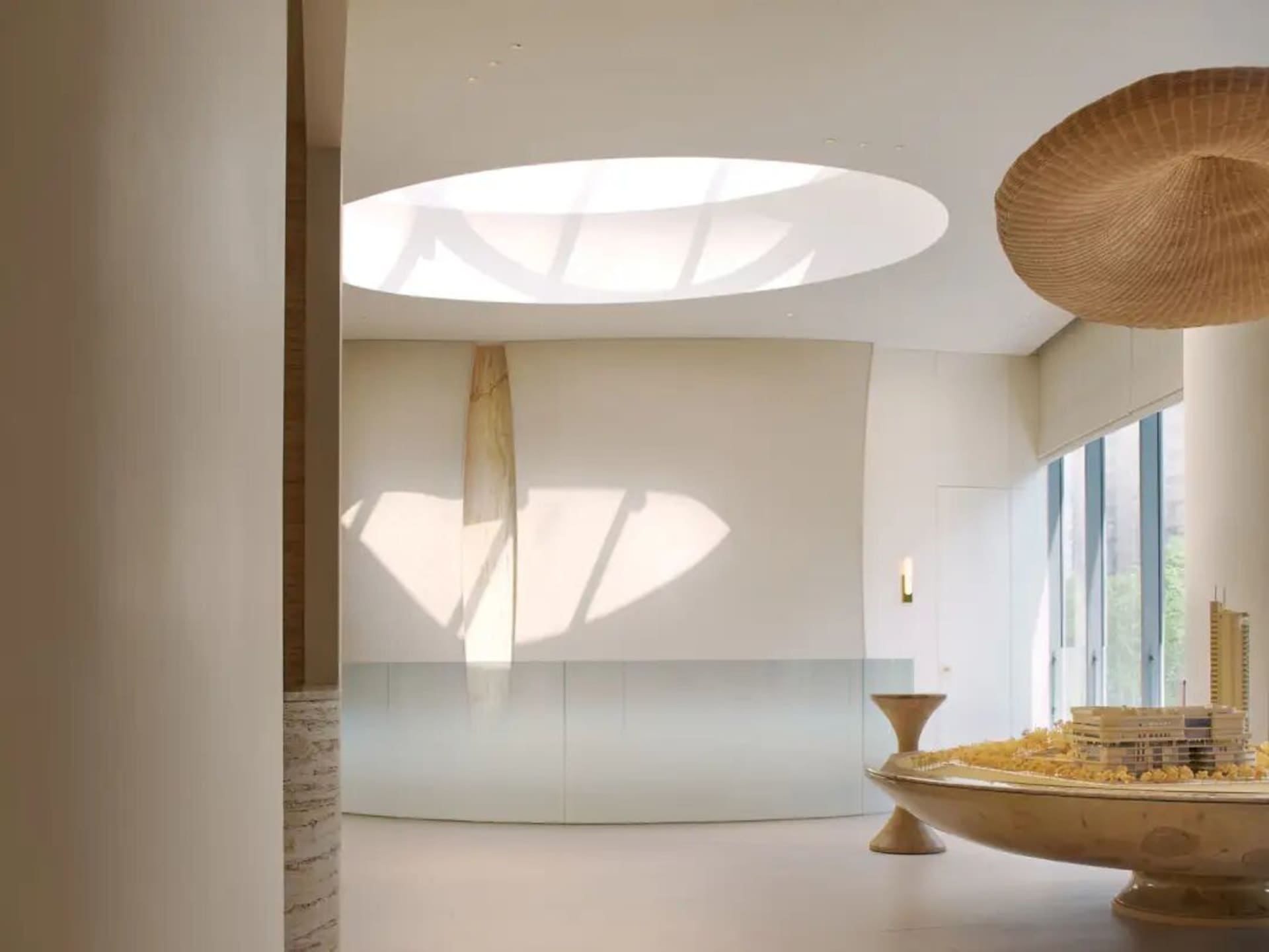 A cozy living space with a wooden table and a large wooden bowl, surrounded by a white color scheme and natural light from a large window