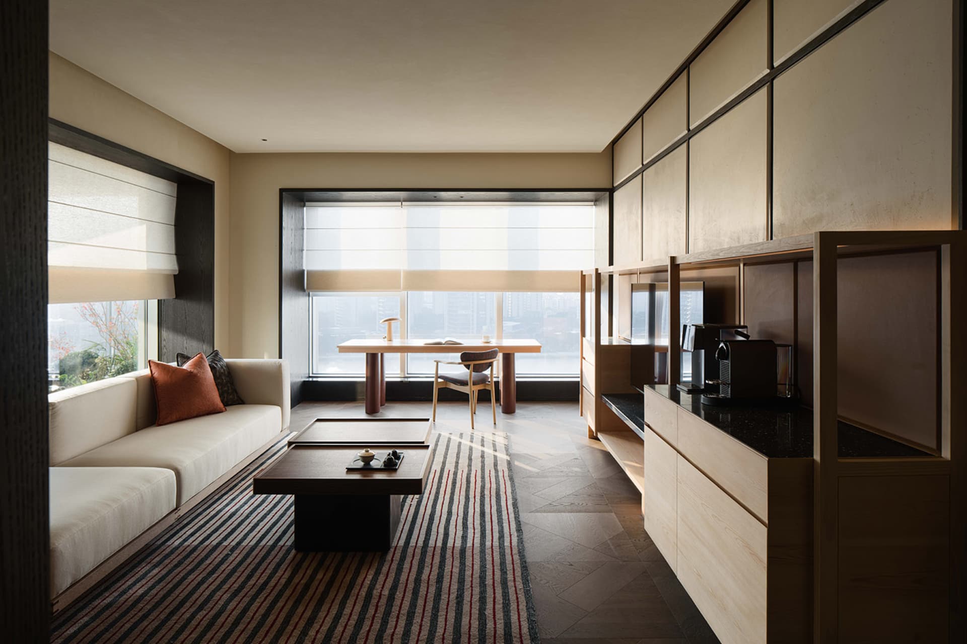 A well-lit modern living room with a couch, coffee table, dining table, and kitchen area, featuring wood furniture and a focus on functionality and comfort