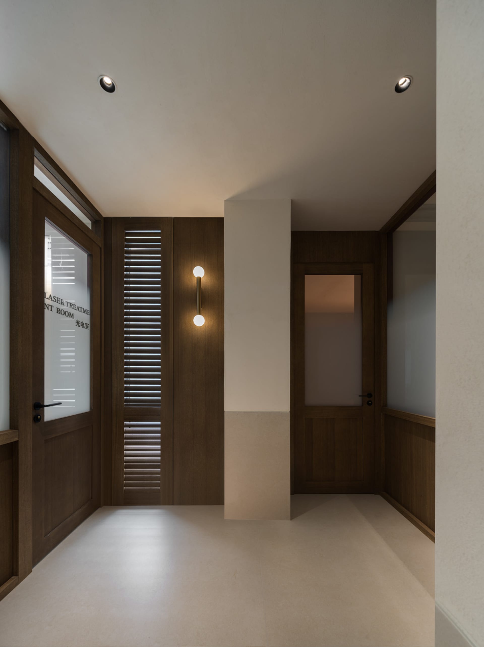 A well-lit hallway with a wooden floor and white walls, featuring an open doorway and a window on the left side