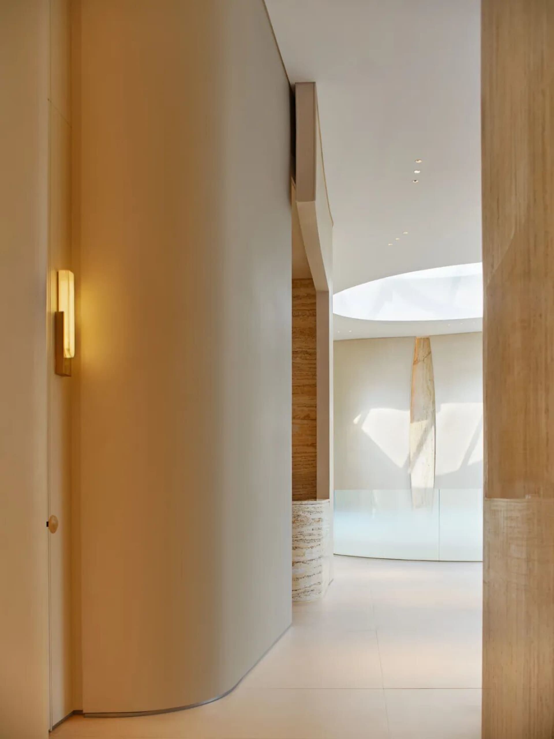 A modern hallway with white marble floors and walls, adorned with artwork, in a dimly lit space with a warm atmosphere