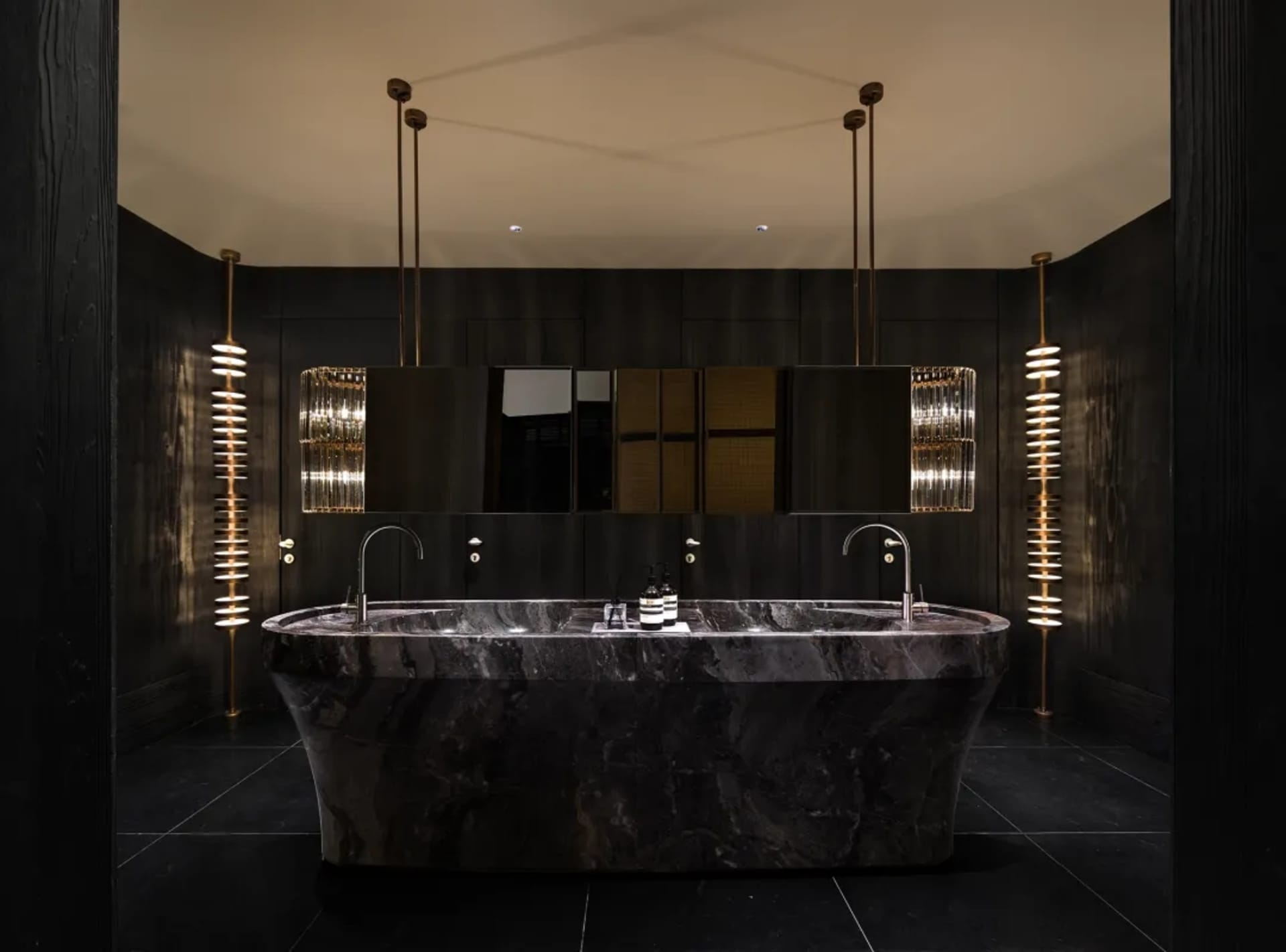 A dimly lit modern bathroom with a large marble bathtub, sink, and mirror