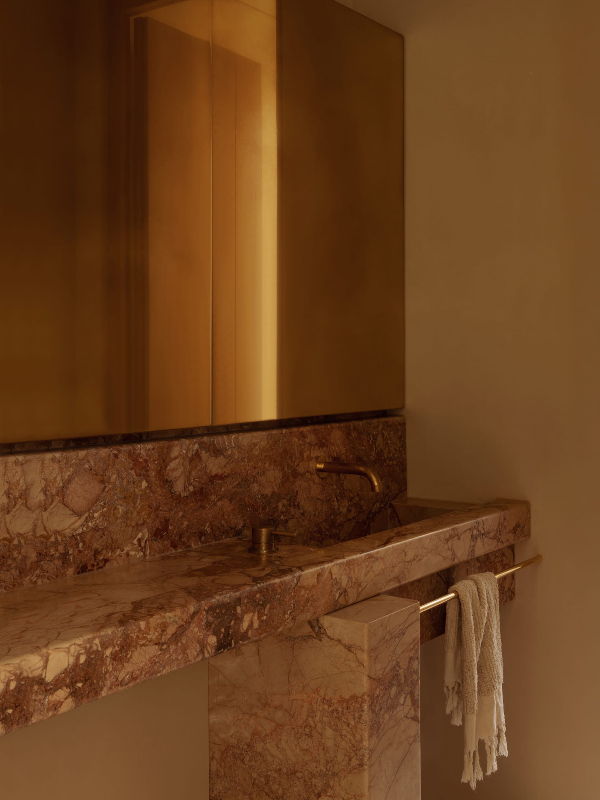Bathroom with a marble sink, gold faucet, and gold-toned mirror in an elegant and luxurious setting with soft warm lighting