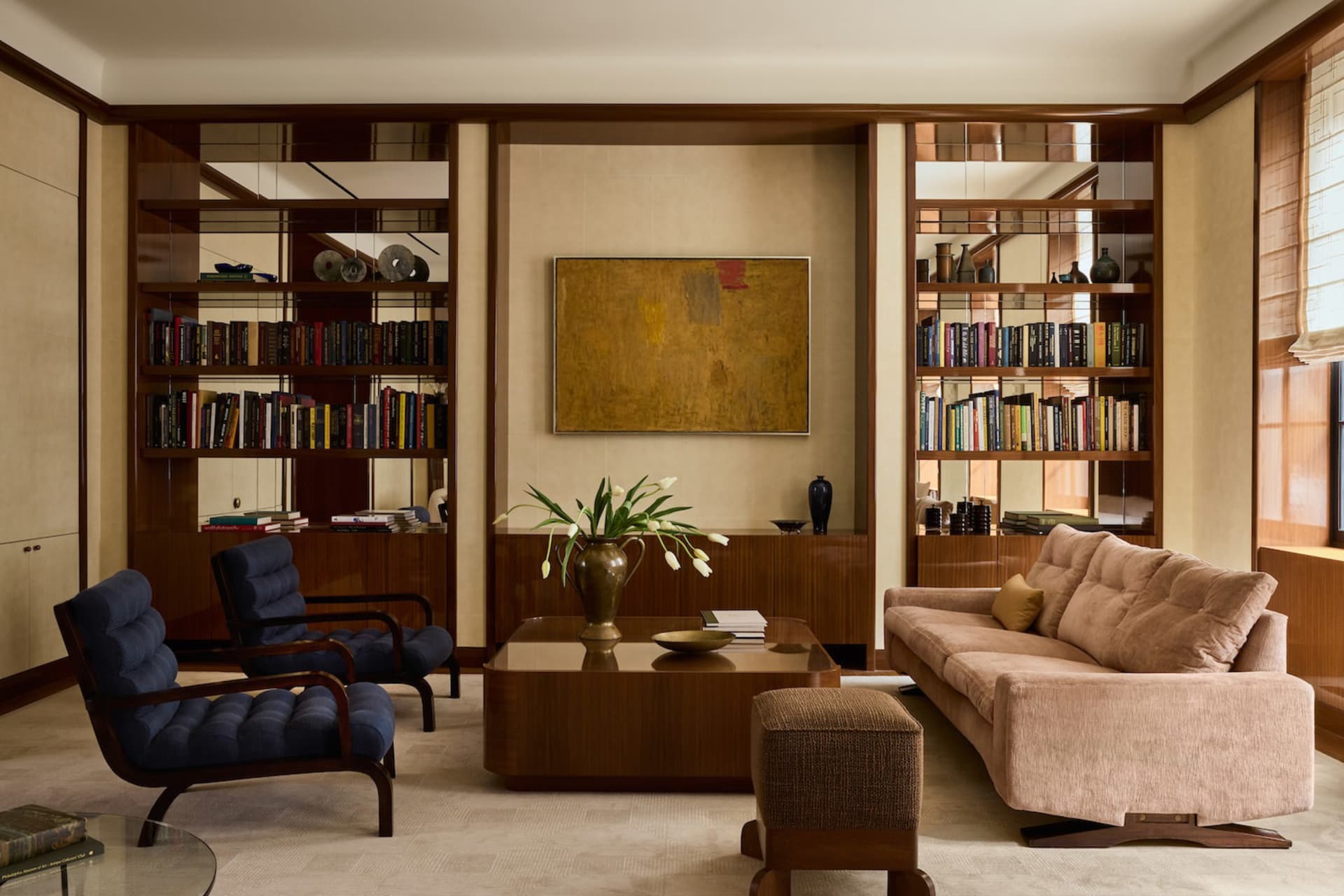 Comfortable living space with a couch, chair, coffee table, books, vases, and potted plants, filled with natural light and warm colors