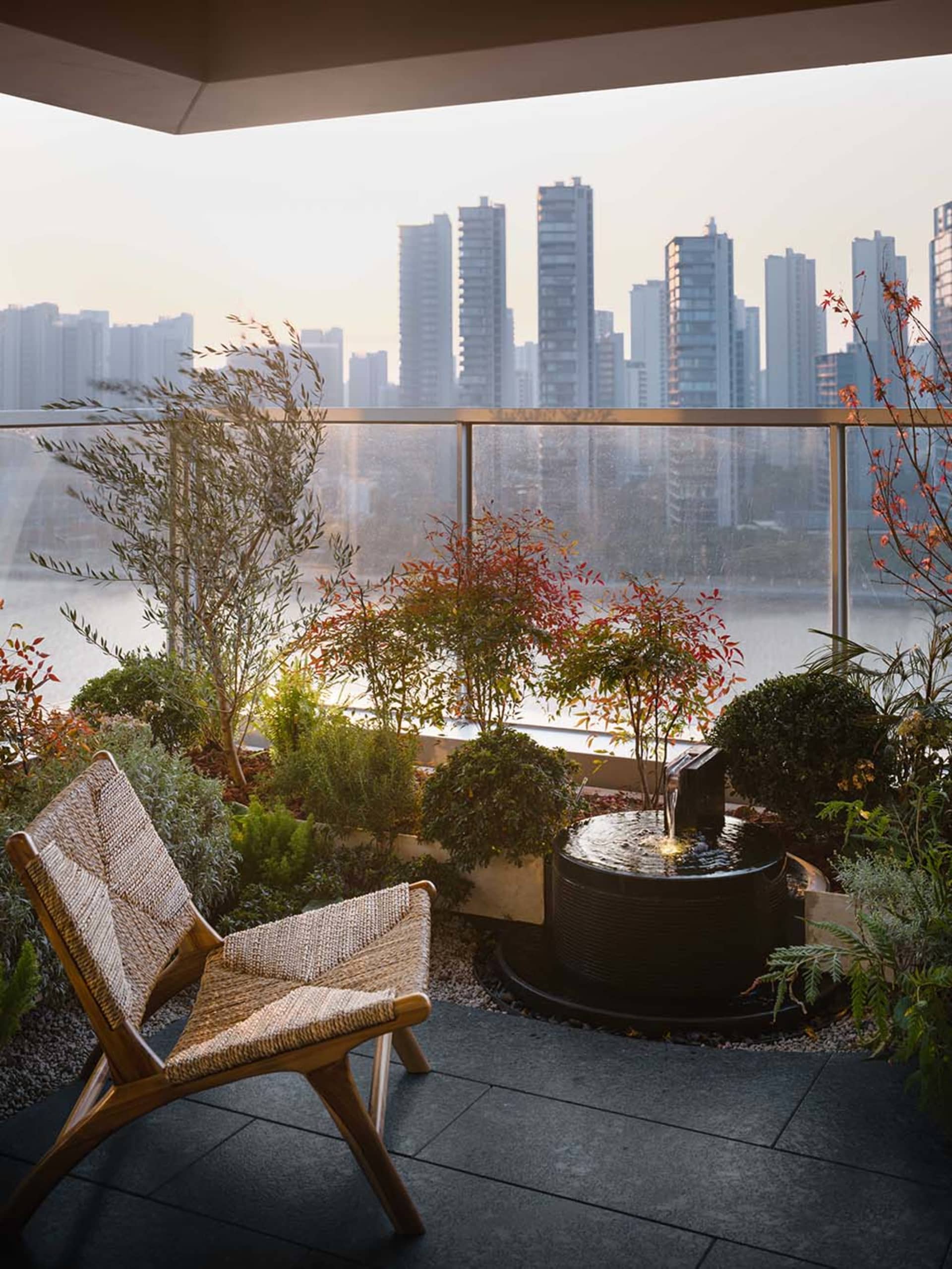A modern living room with a large window overlooking the city, featuring a couch, chair, dining table, and potted plants, with a mix of wood, glass, and metal materials