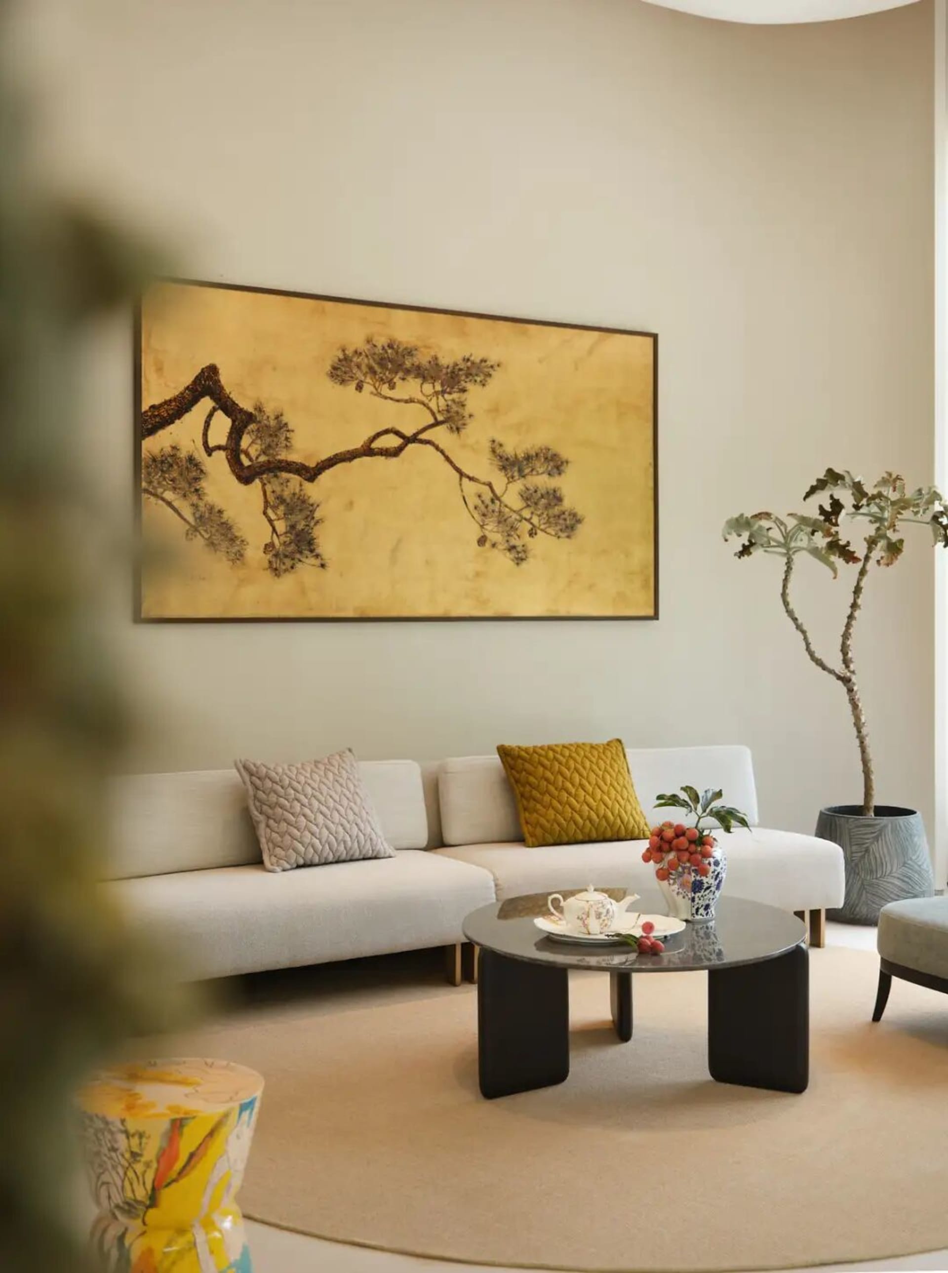 A well-lit modern living room with a white couch, a black coffee table, and a large oriental painting on the wall, creating a bright and inviting atmosphere