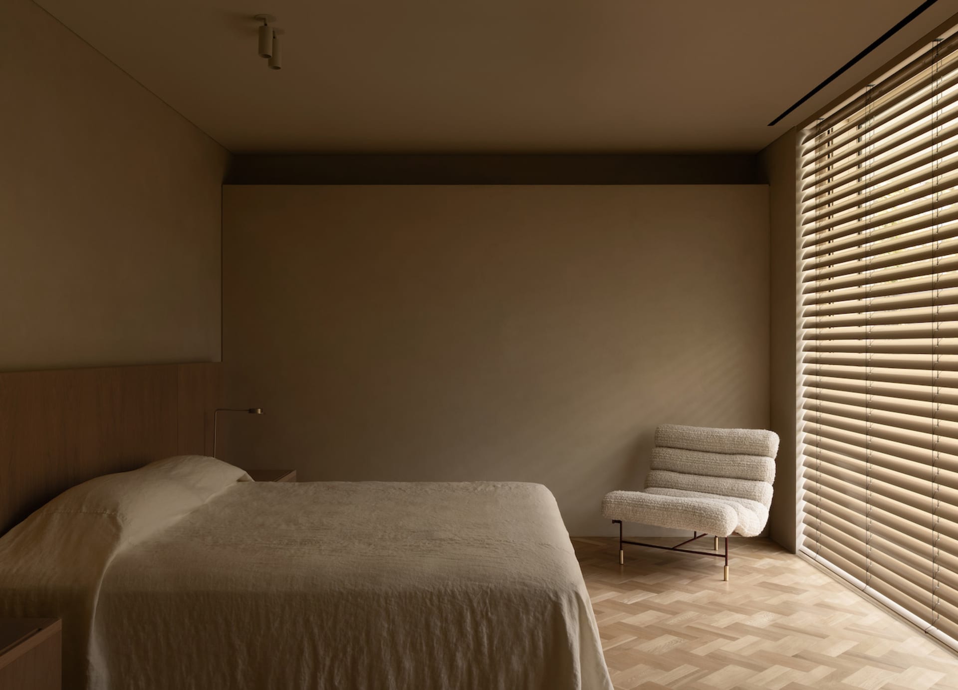A calm and inviting bedroom with a bed, chair, and window, featuring a mix of modern and traditional styles, neutral colors, and wooden elements, with natural light streaming in through the window