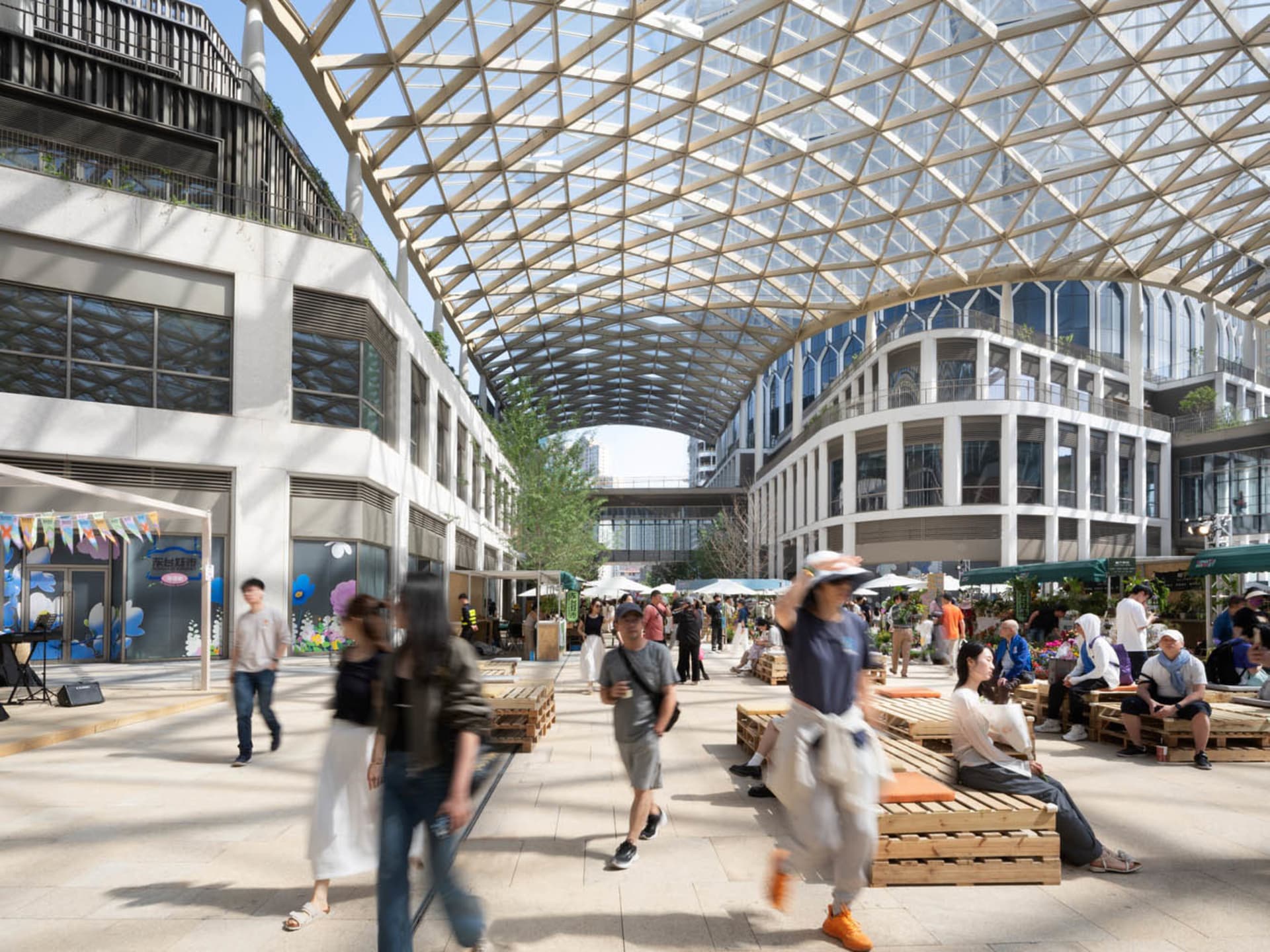 A large, open public space with a glass ceiling, numerous pillars, and a lively atmosphere, filled with people walking, sitting, and engaging in activities