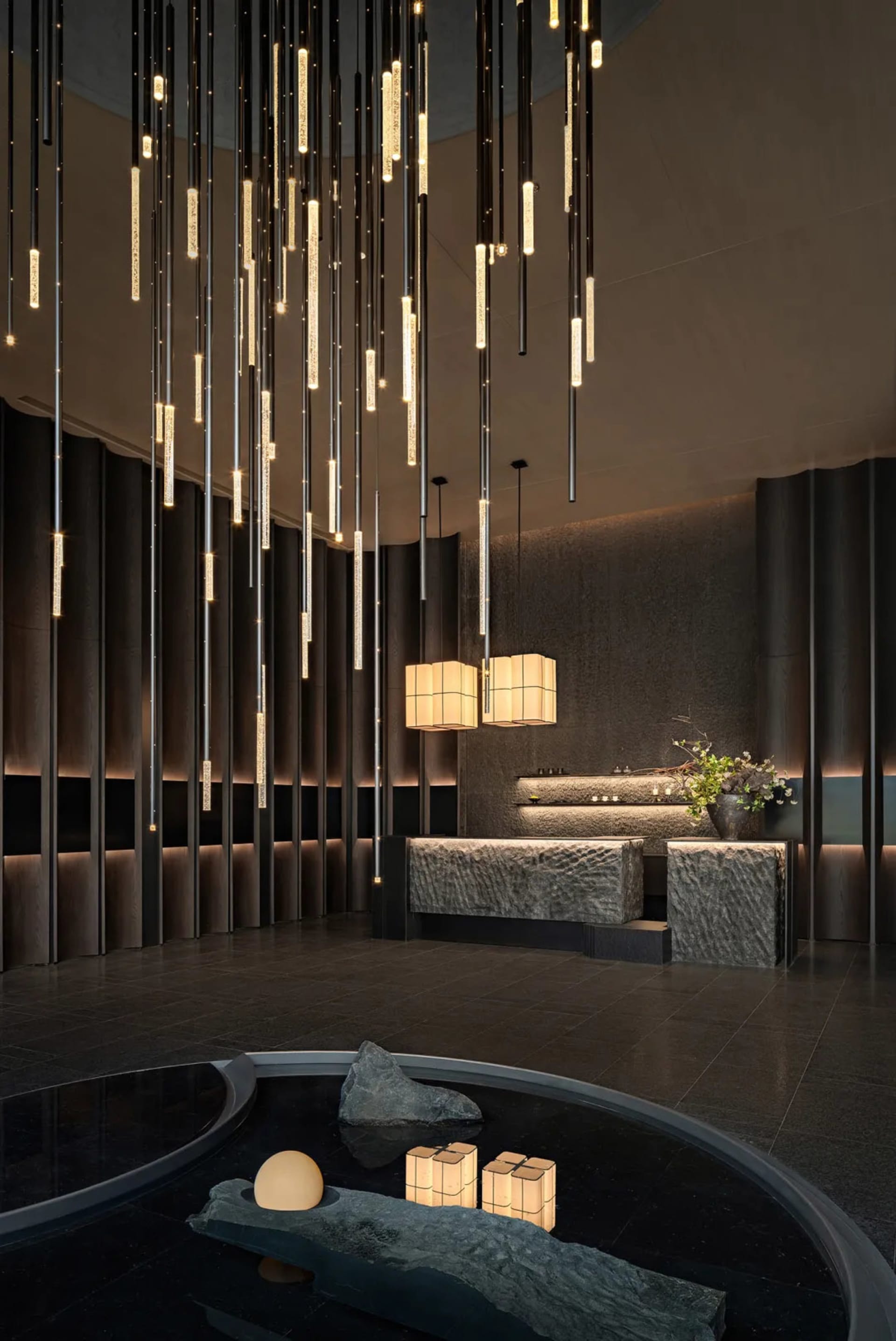 A well-lit modern living room with a chandelier, stone and wood walls, a couch, and a dining table