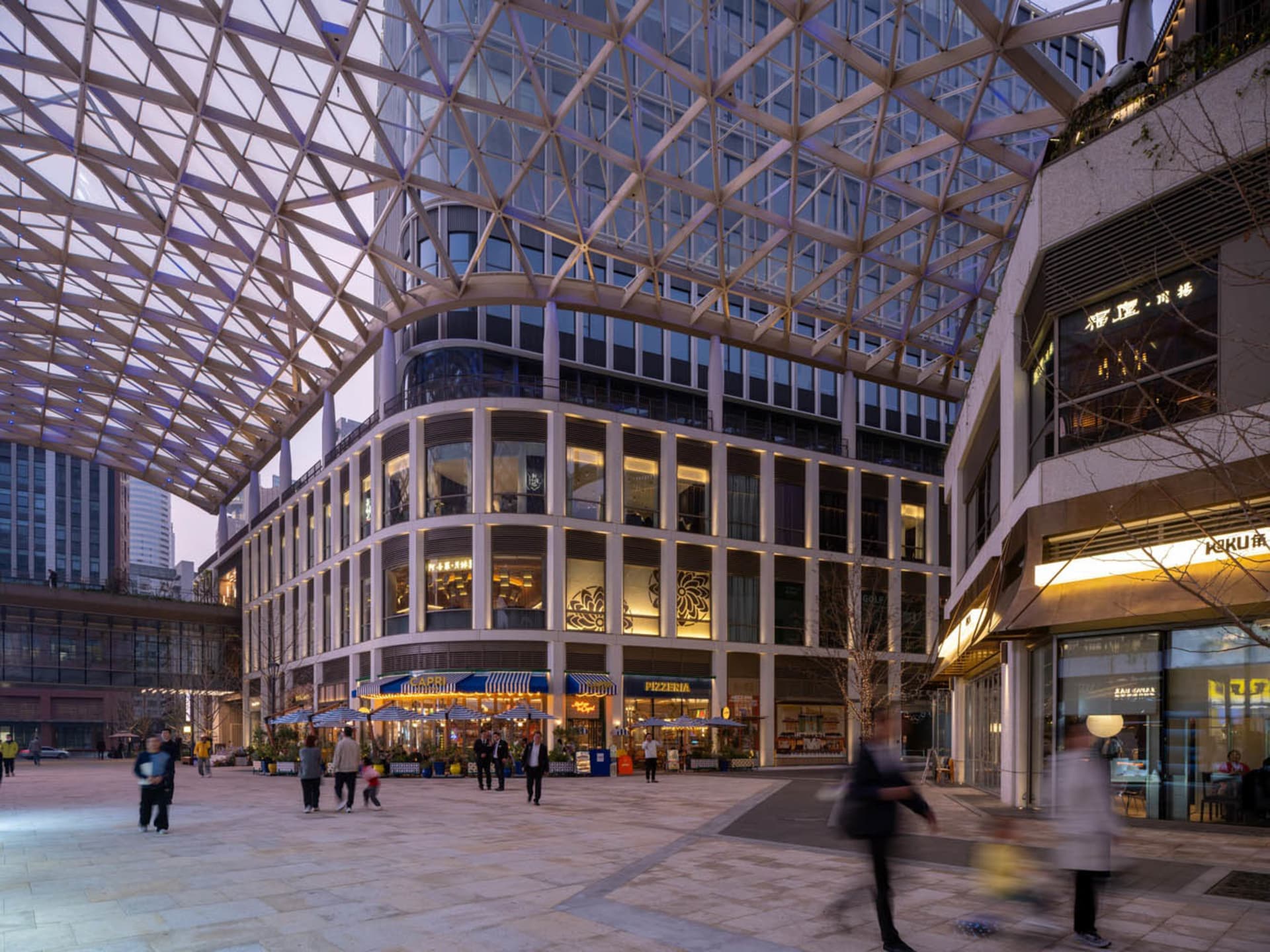 A bustling city street at night with a large building featuring a glass ceiling, surrounded by people and artificial lighting