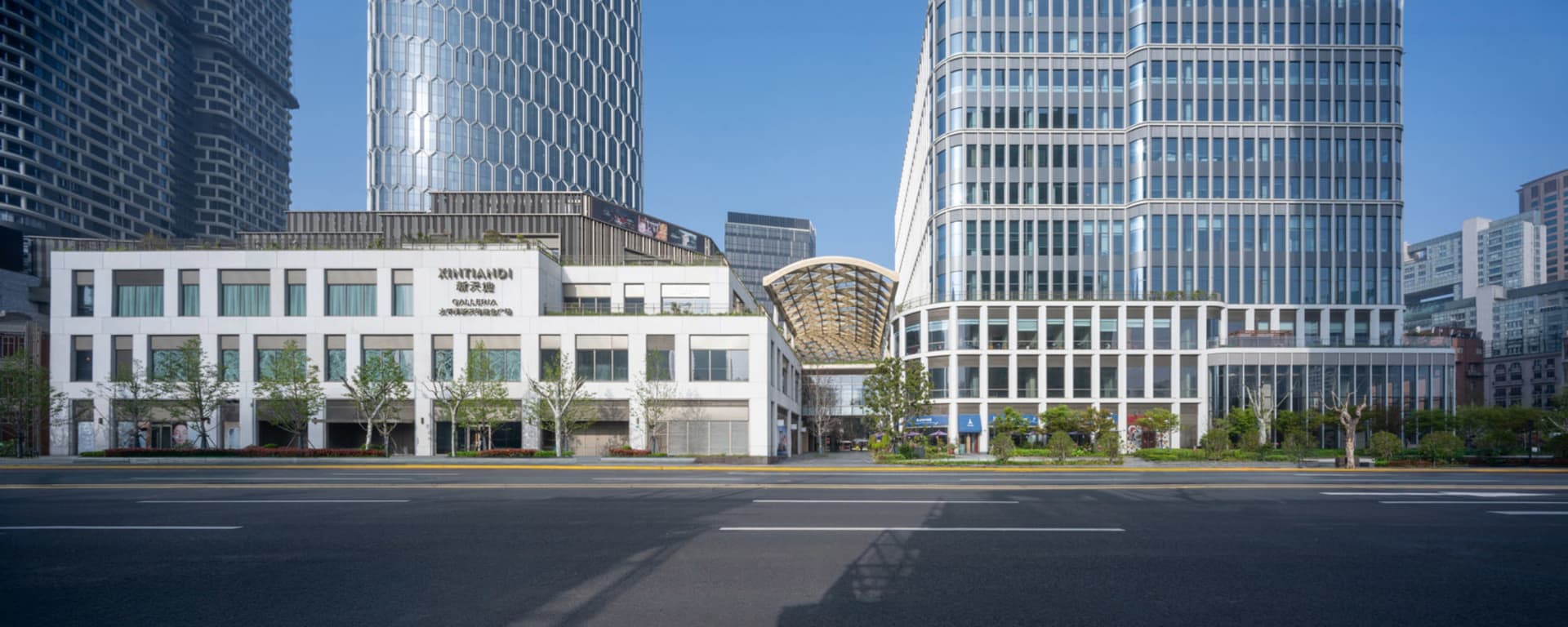 A city street lined with tall glass and steel buildings, surrounded by trees, creating a calm and peaceful atmosphere