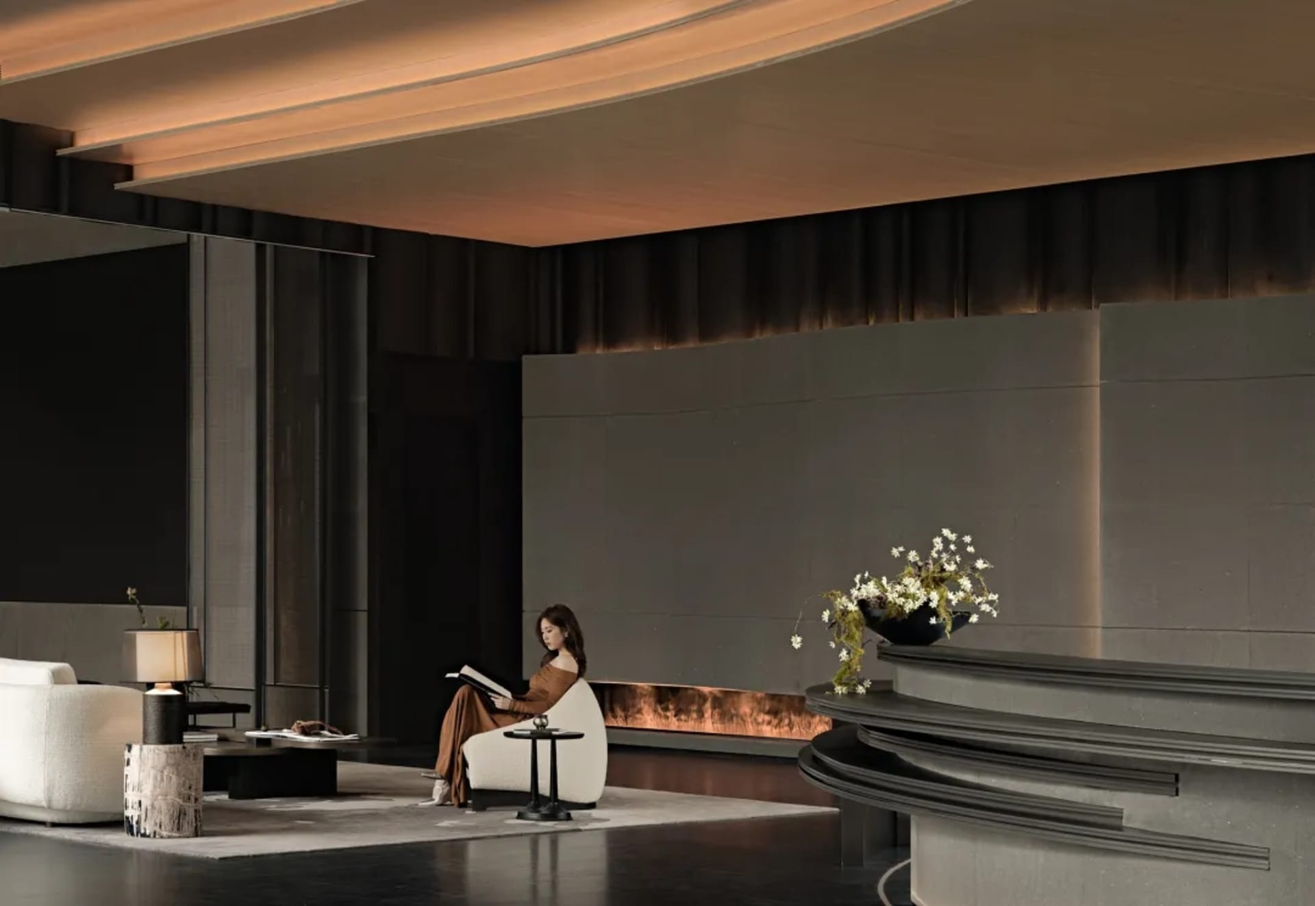 A woman sits on a couch in a modern living room with a chair and dining table, surrounded by black and white elements and a vase with flowers