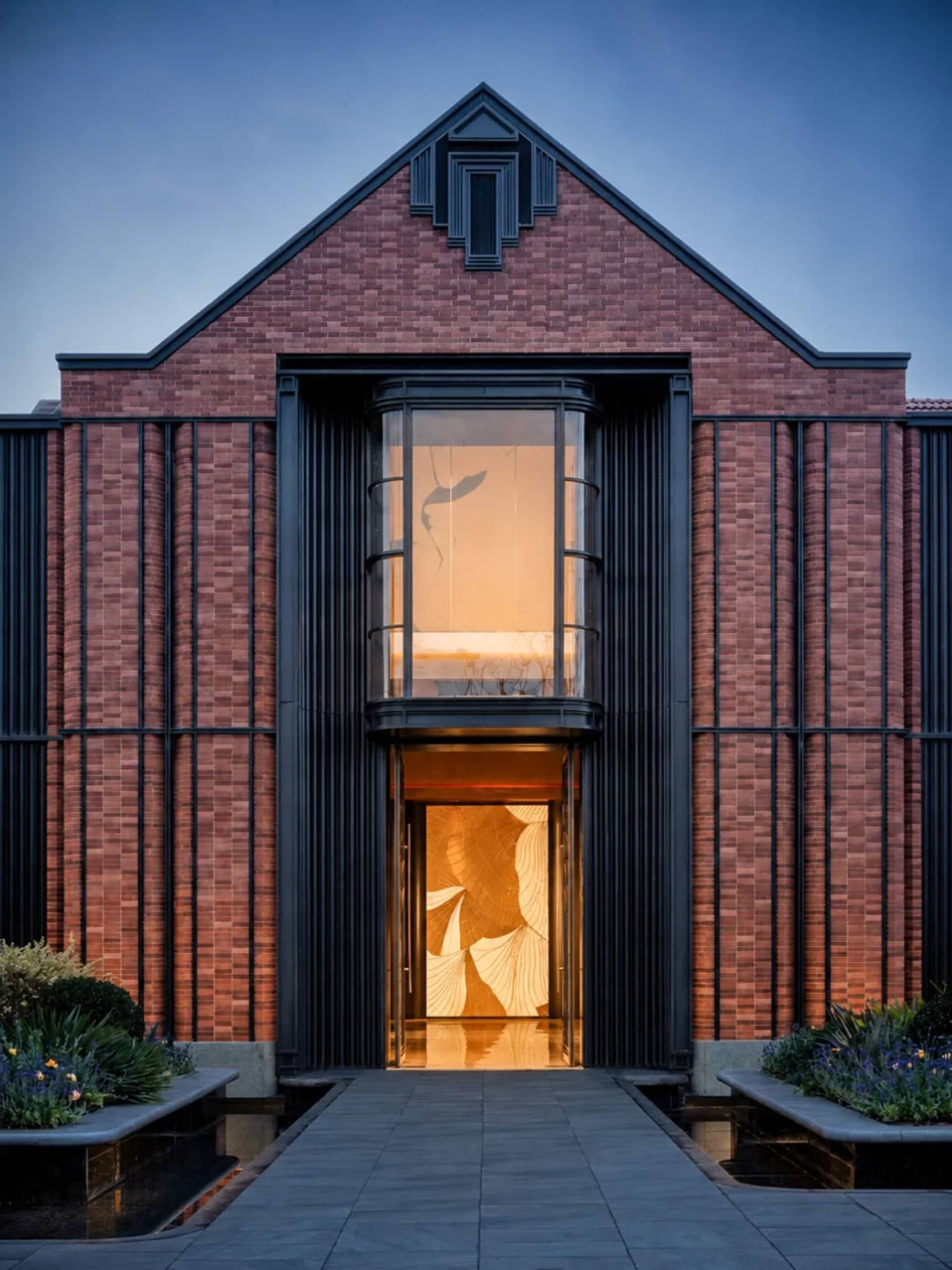 A modern church with a red brick facade, arched doorway, and glass elements, set against a soft and warm background