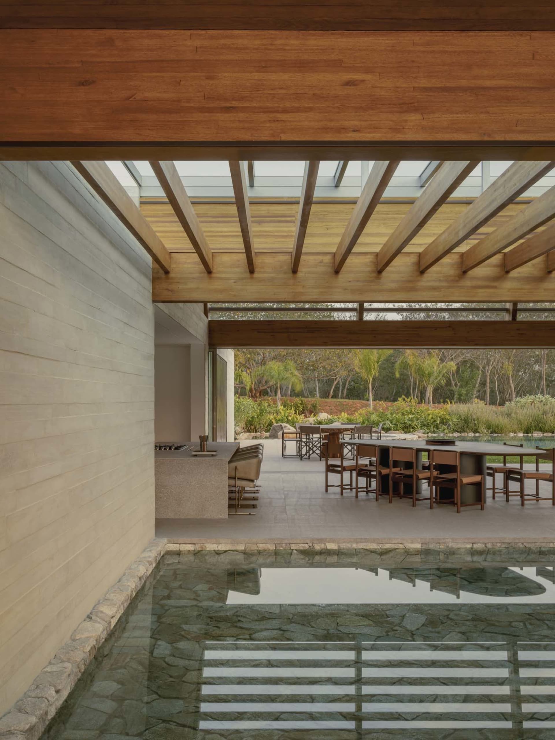 Large open living space with a pool and dining area, surrounded by furniture, wood, and stone, with natural light and a relaxed atmosphere