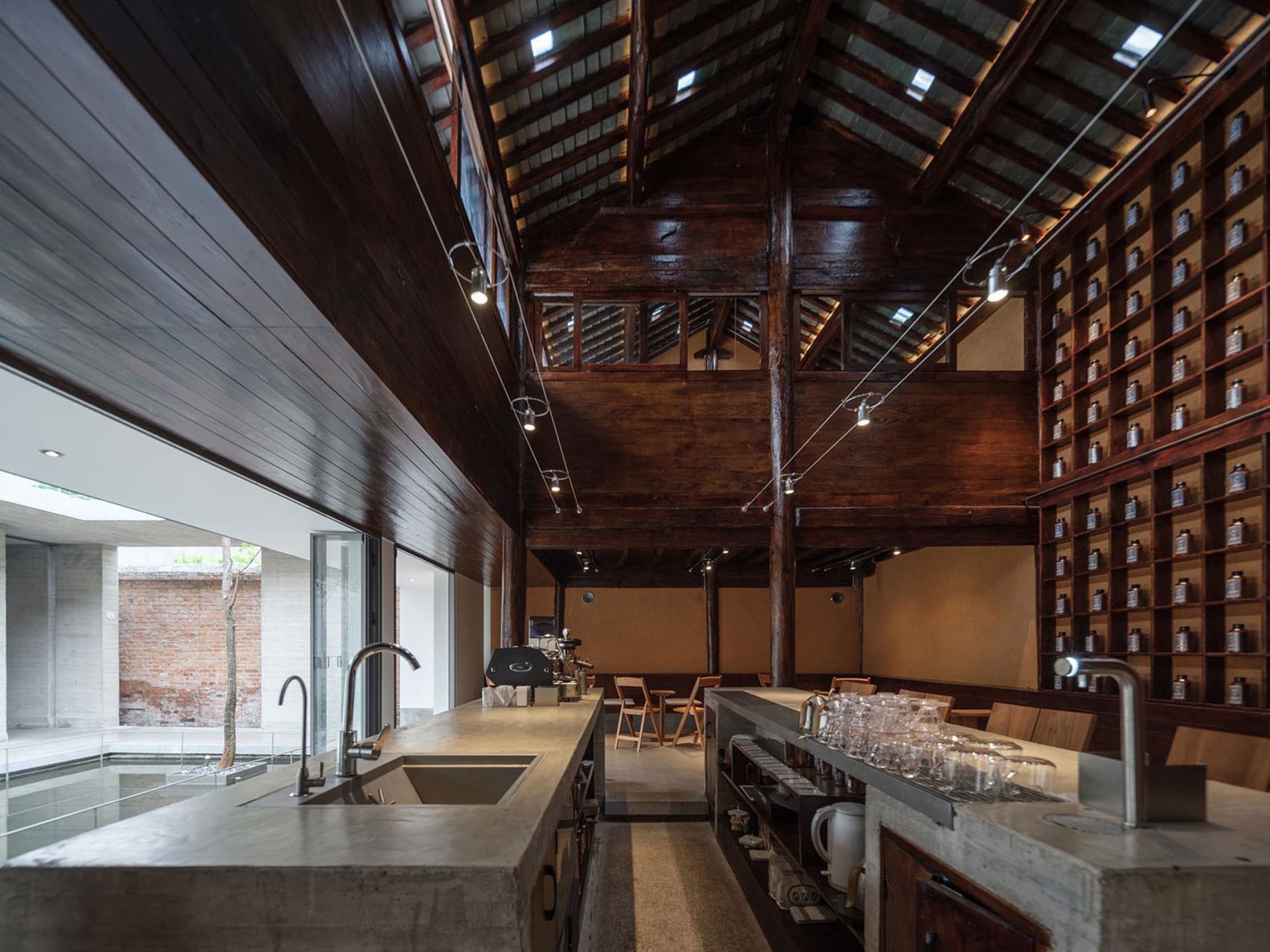 Open kitchen dining space with wooden floors, high ceiling, sink, dining table, and chairs, lit by natural sunlight