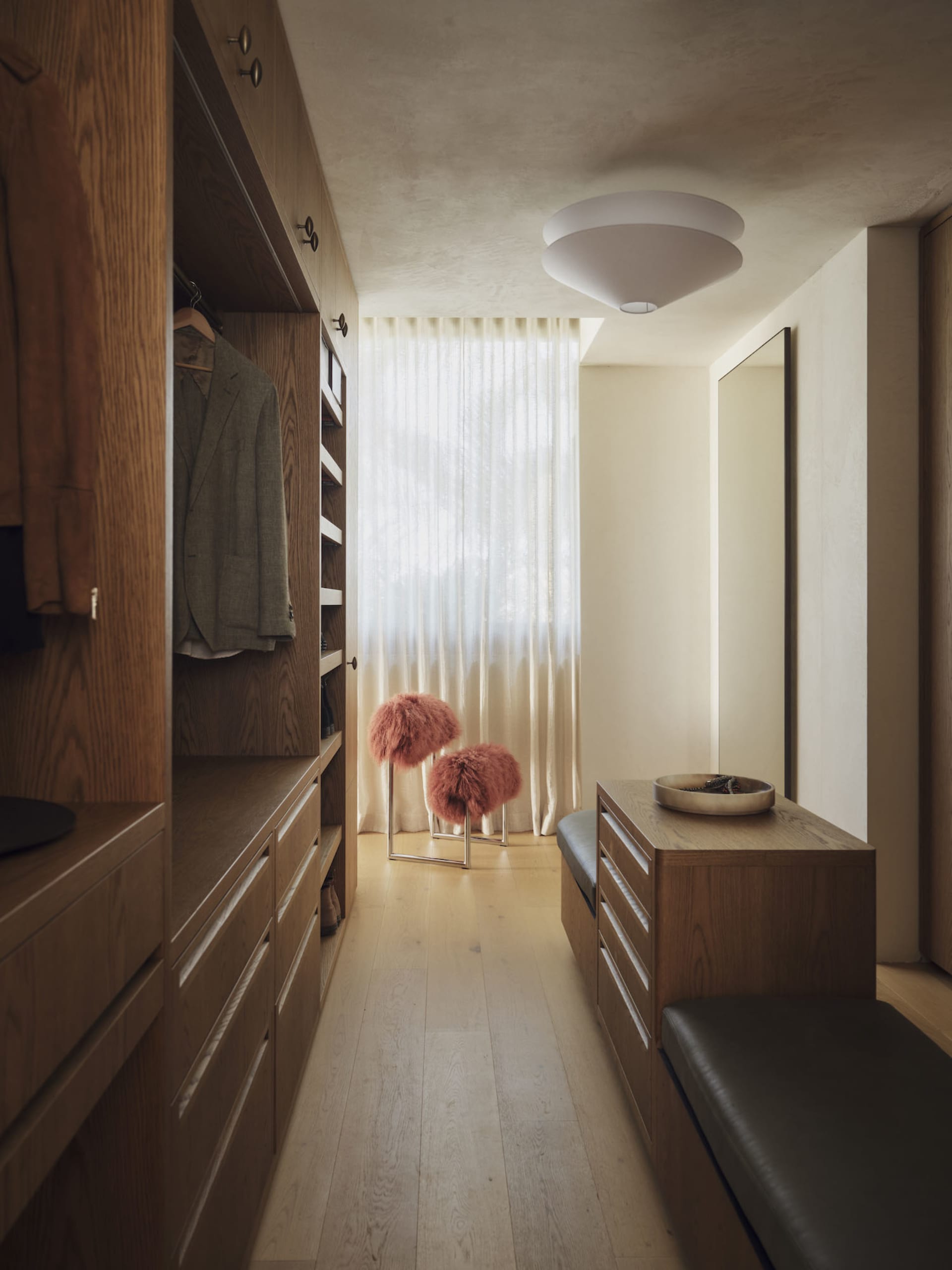 Cozy modern bedroom with a wooden floor, white wall, and dim lighting, featuring a bench and two pink feathered objects