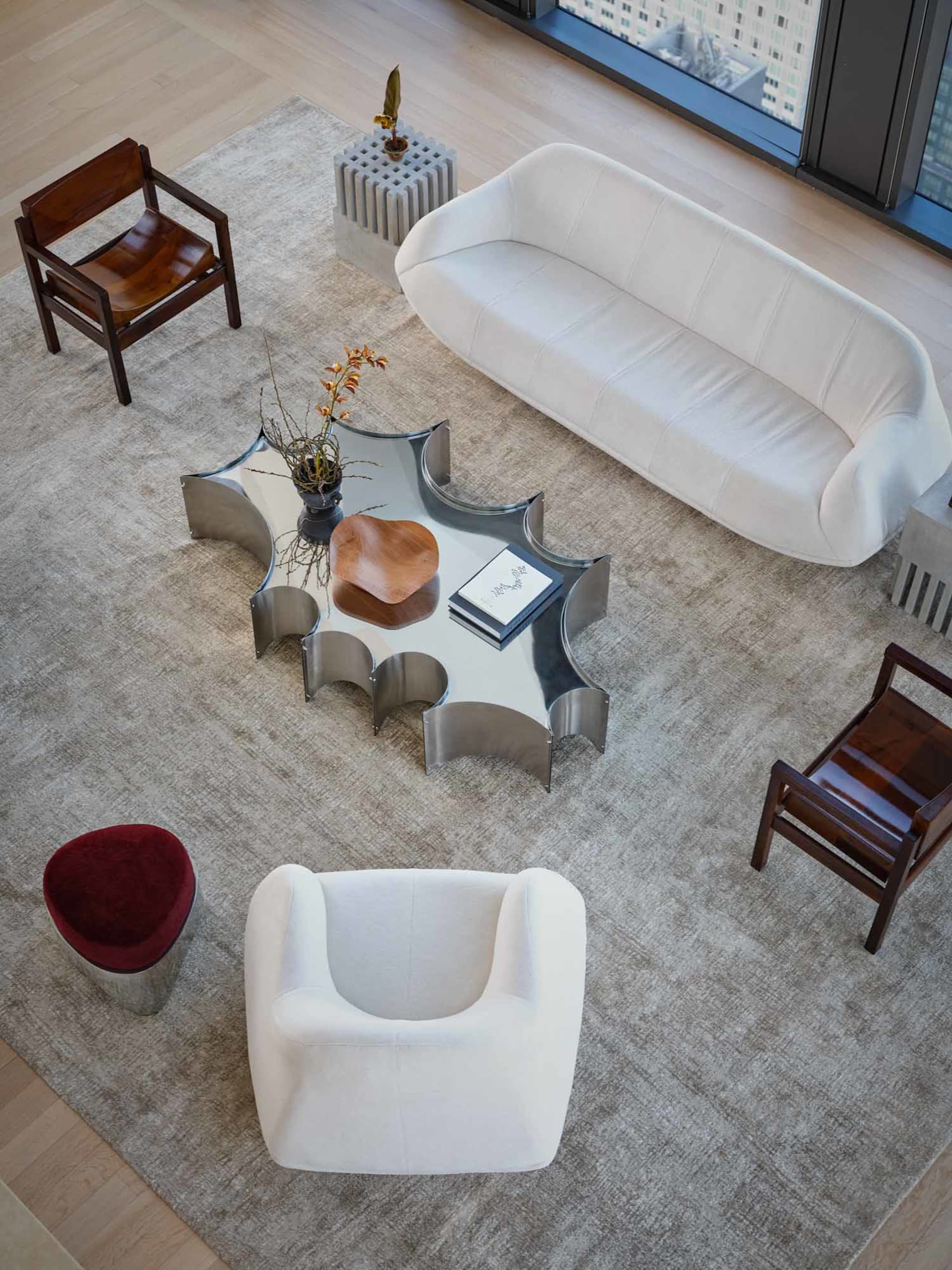 Cozy modern living space with a white couch, chair, and coffee table, surrounded by books and a rug, with natural light from a window