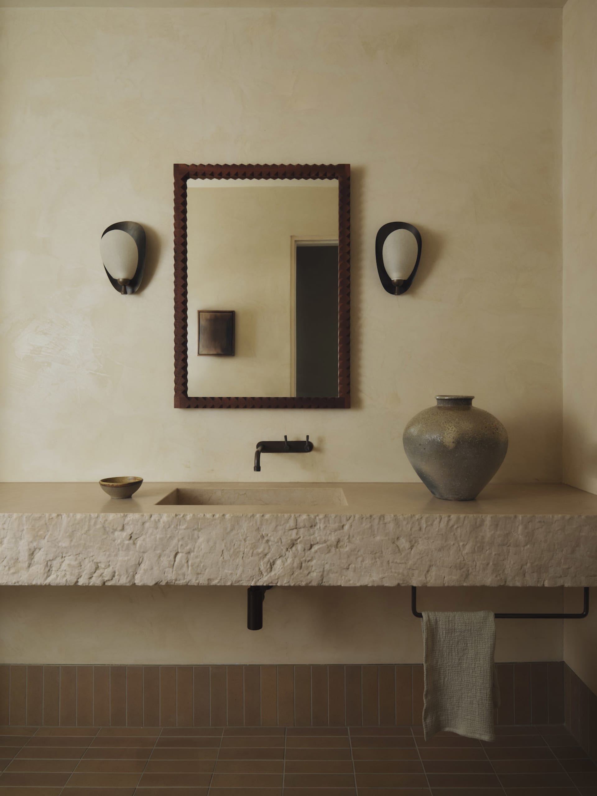 Cozy bathroom with a brown color scheme, featuring a sink, mirror, and vase, under dim lighting