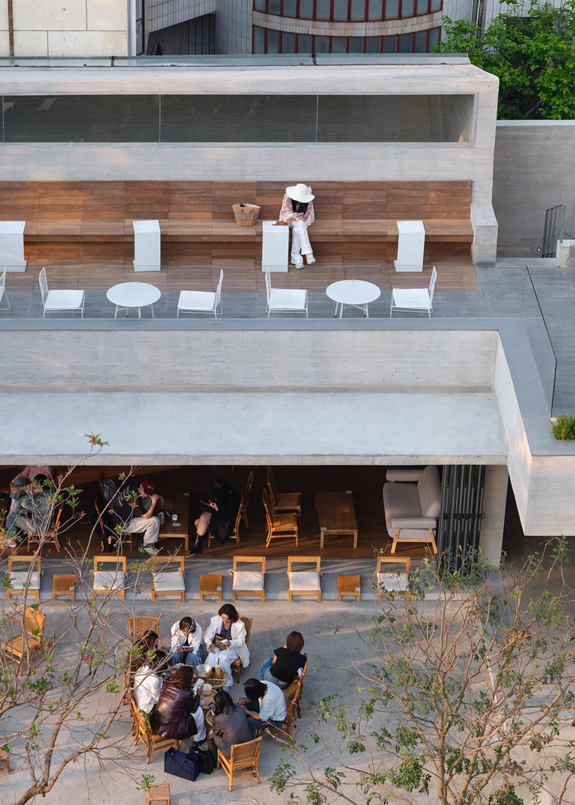 A casual outdoor restaurant with wooden furniture, a woman sitting on a bench, and other people in the scene