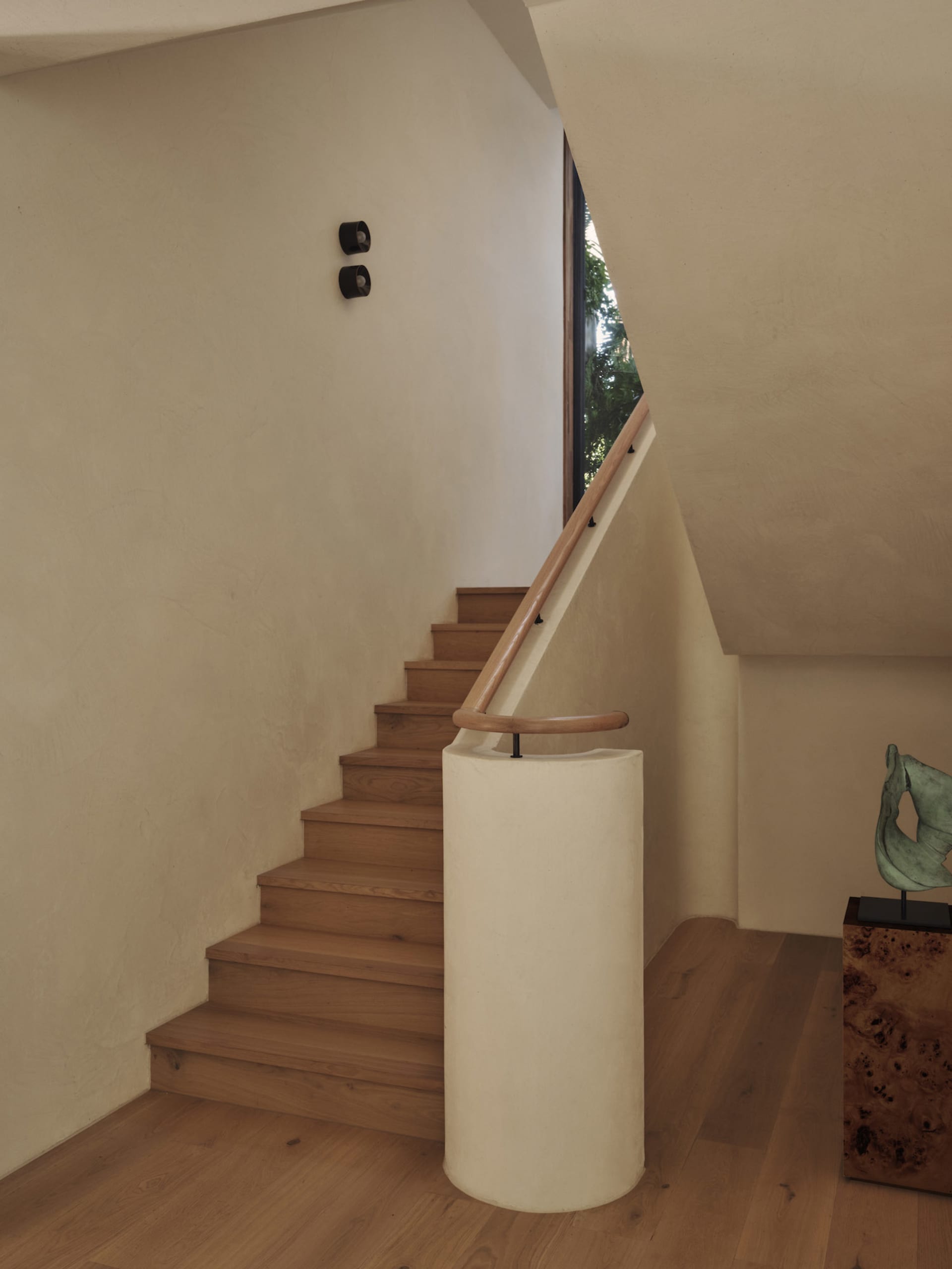 A wooden staircase with a white railing in a bright and welcoming hallway with a nearby window