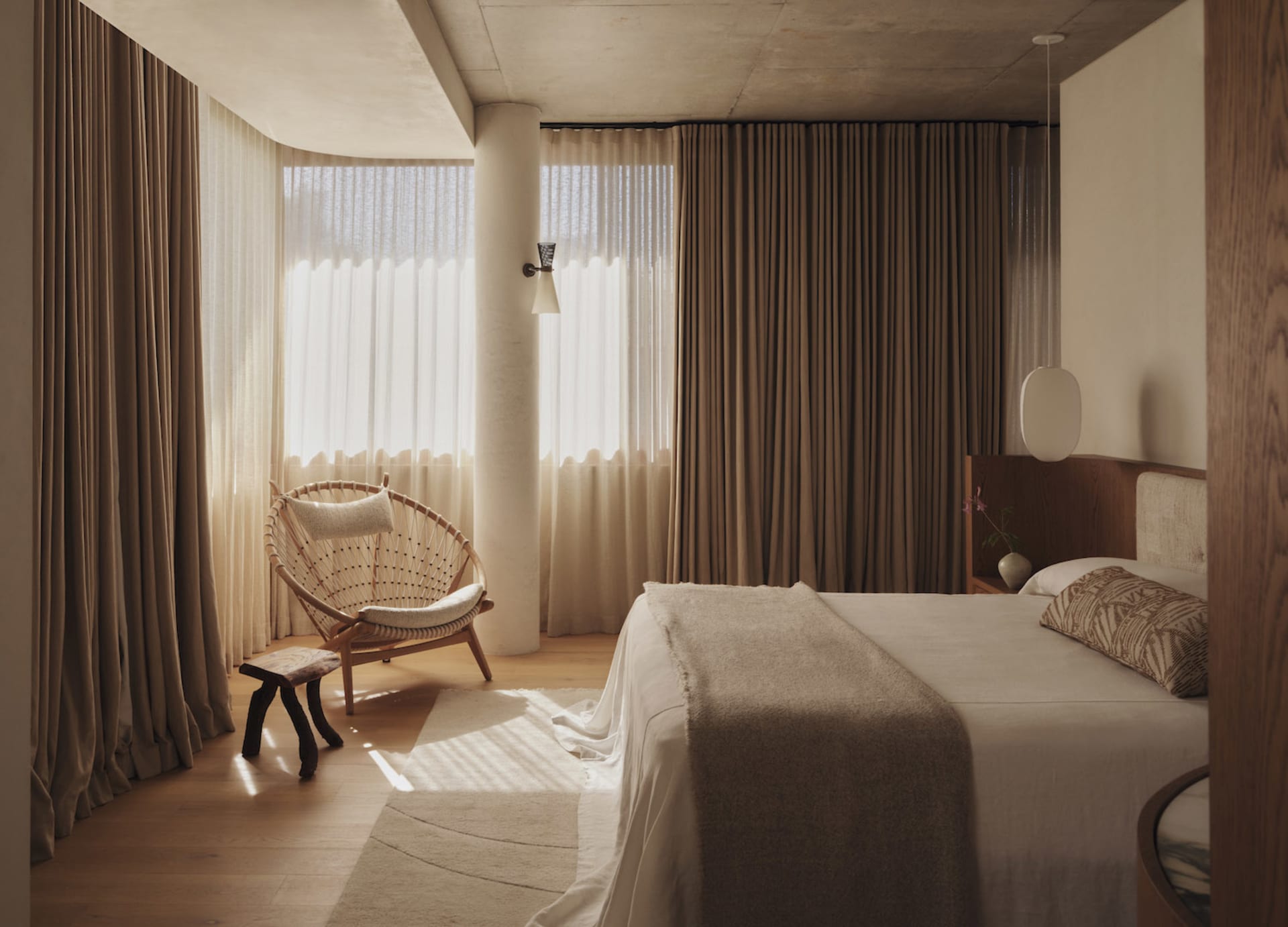 A well-lit bedroom with a bed against the wall, a chair near the window, and a modern design featuring white walls and a wooden floor