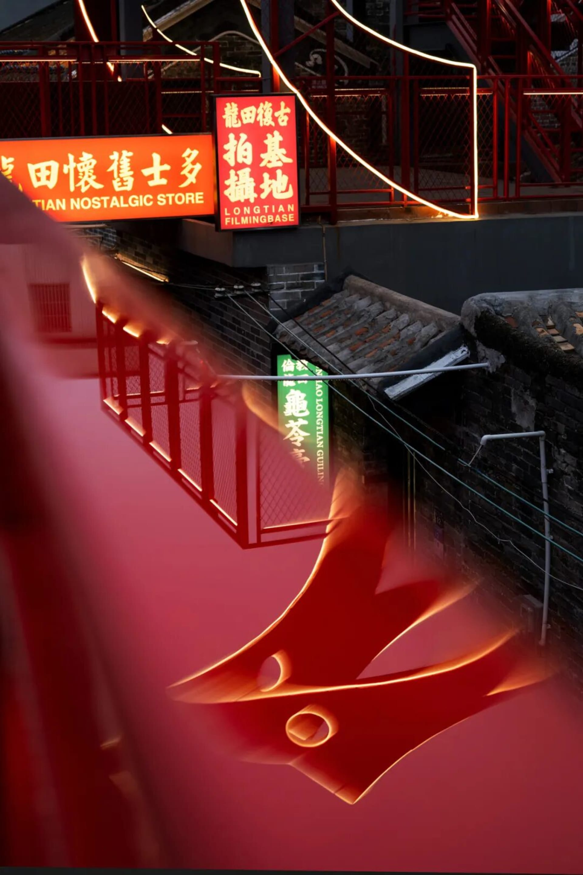 A storefront with a red and orange color scheme, illuminated by lights, and a brick wall in the background, featuring a sign with Chinese characters and a nameplate reading Longlong Antique Store