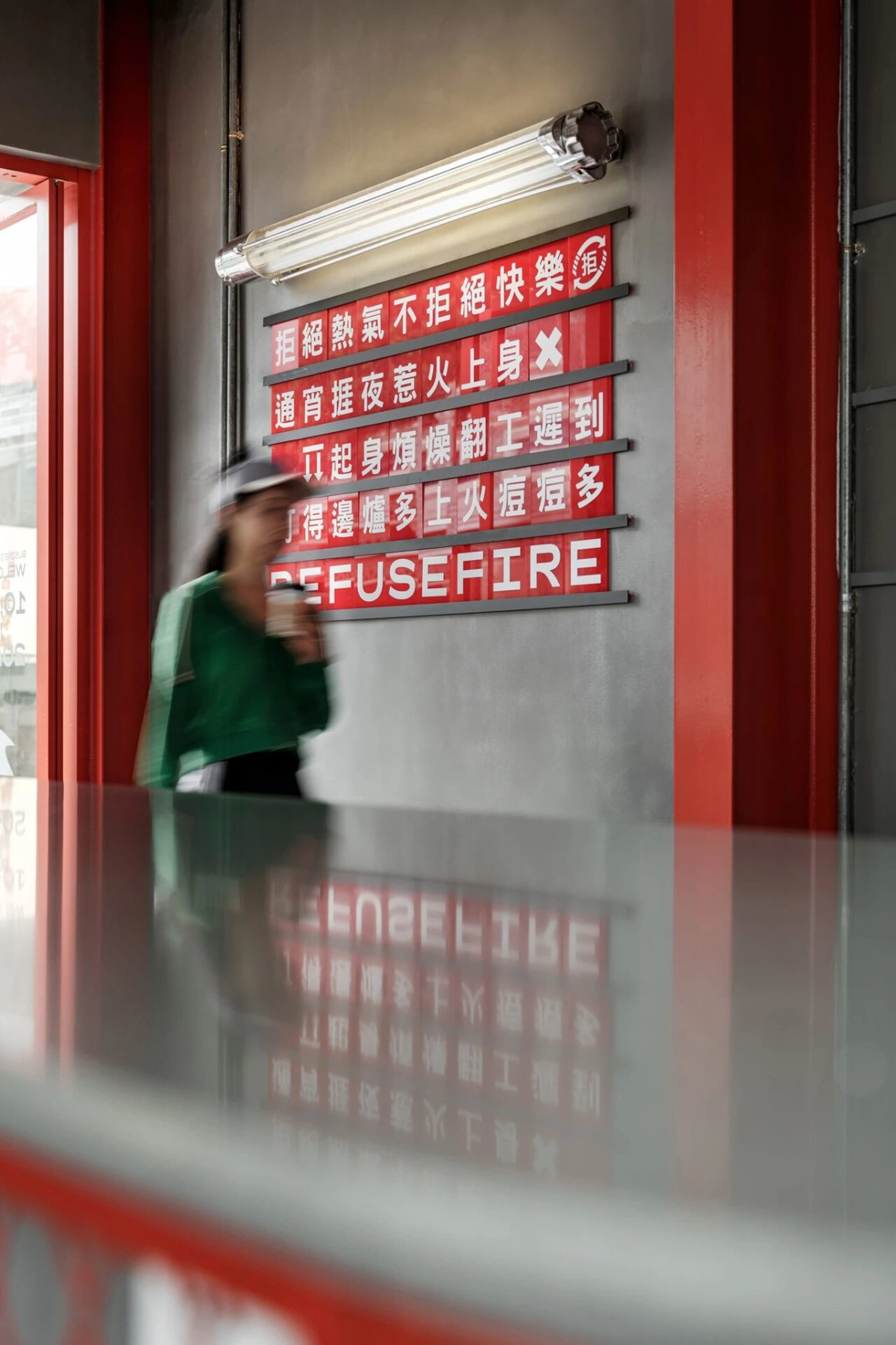 A woman walks past a red wall with foreign language signs in an urban setting