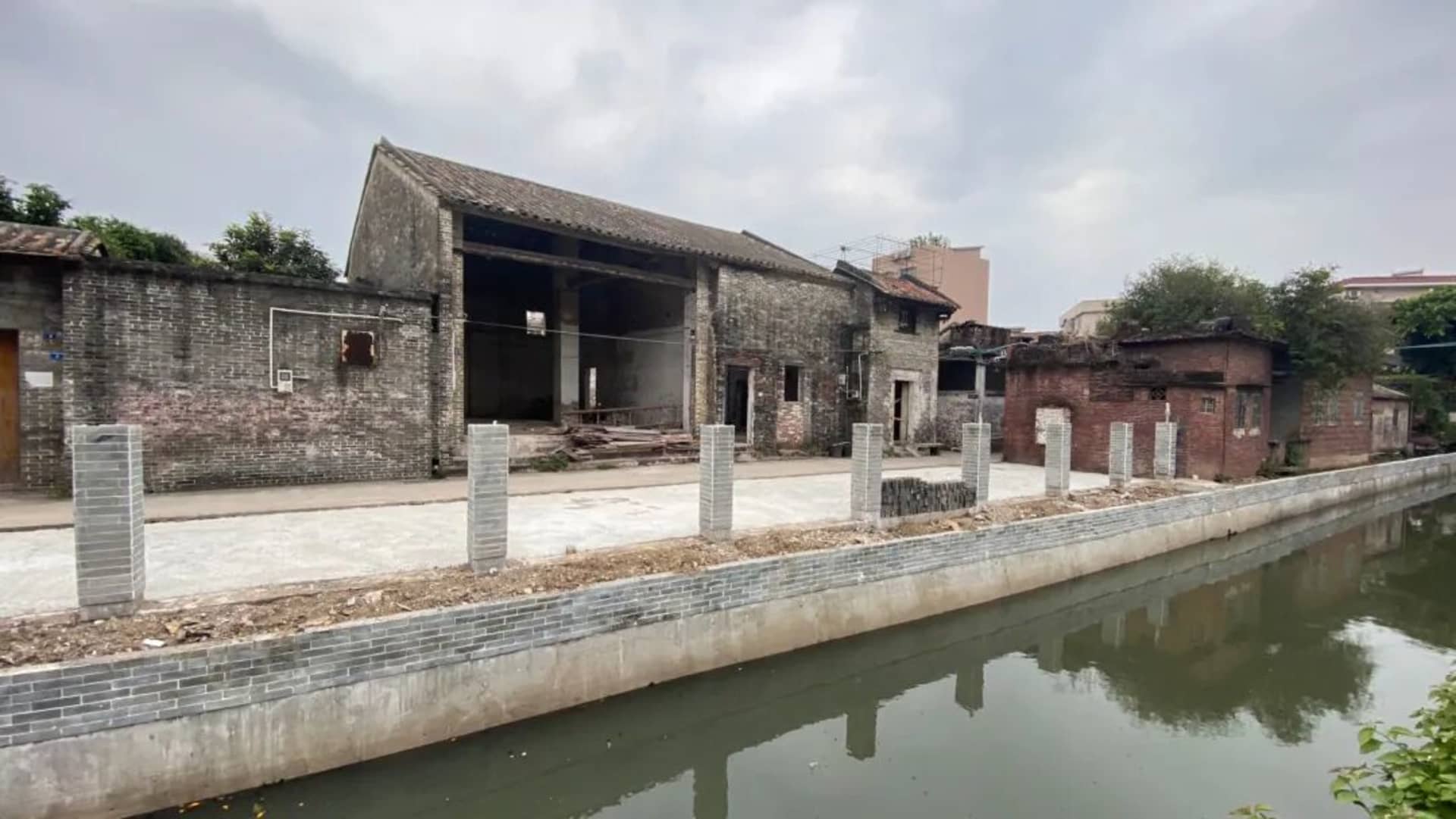 一棟帶有磚牆立面與石材質感的鄉村風建築，緊鄰水域，遠處停泊著一艘小船，營造出寧靜的氛圍
