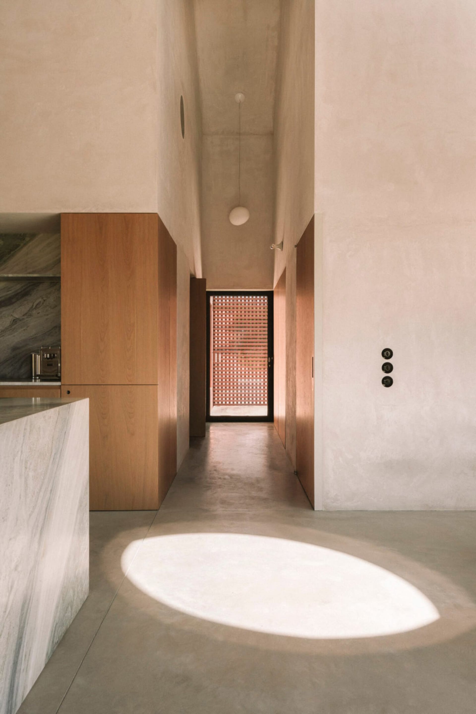 A modern kitchen and hallway area with white surfaces, a kitchen counter, dining table, and natural light from a window