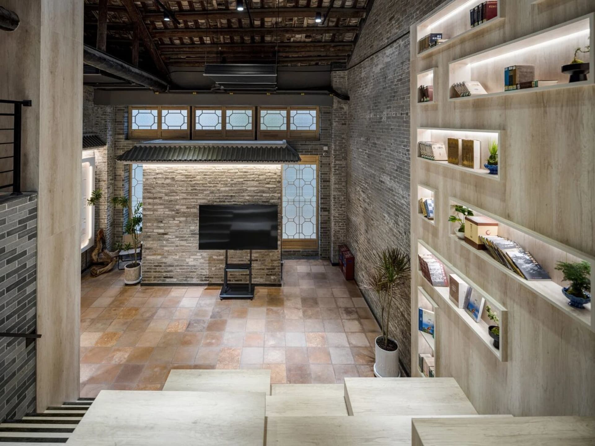 Cozy living room with a brick wall, stone floor, and dim lighting, featuring a flat screen TV, bookshelves, and a potted plant