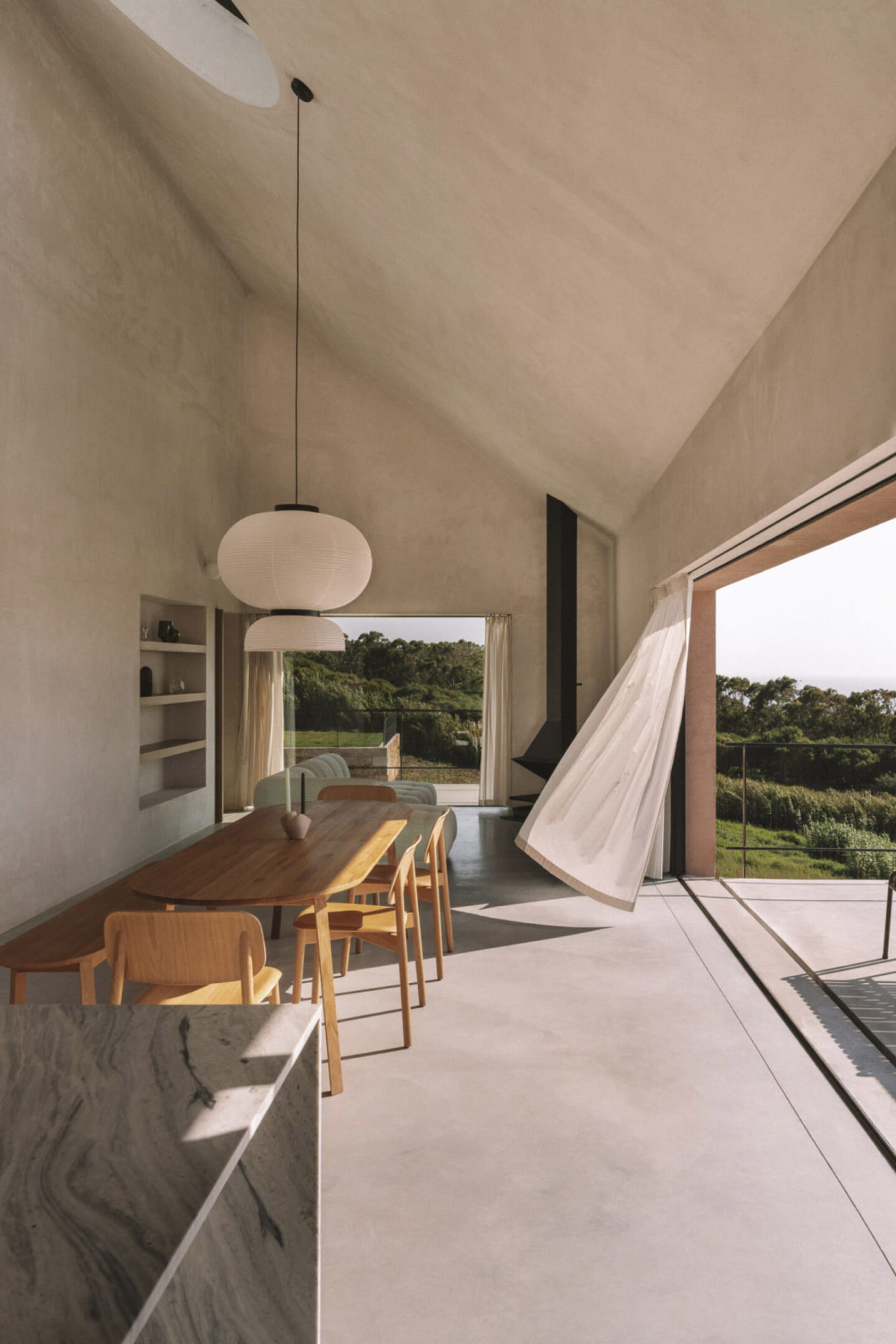 A bright and inviting open-concept living space with a wooden dining table, kitchen with sink and refrigerator, and natural light pouring in