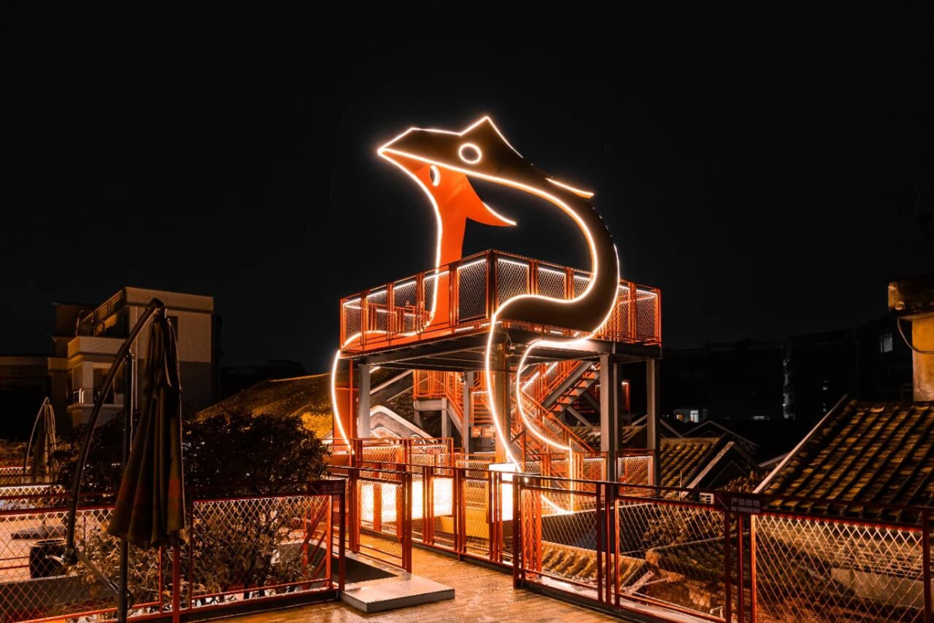 A modern building with a large red metal snake sculpture on its side, captured in a dark and moody atmosphere